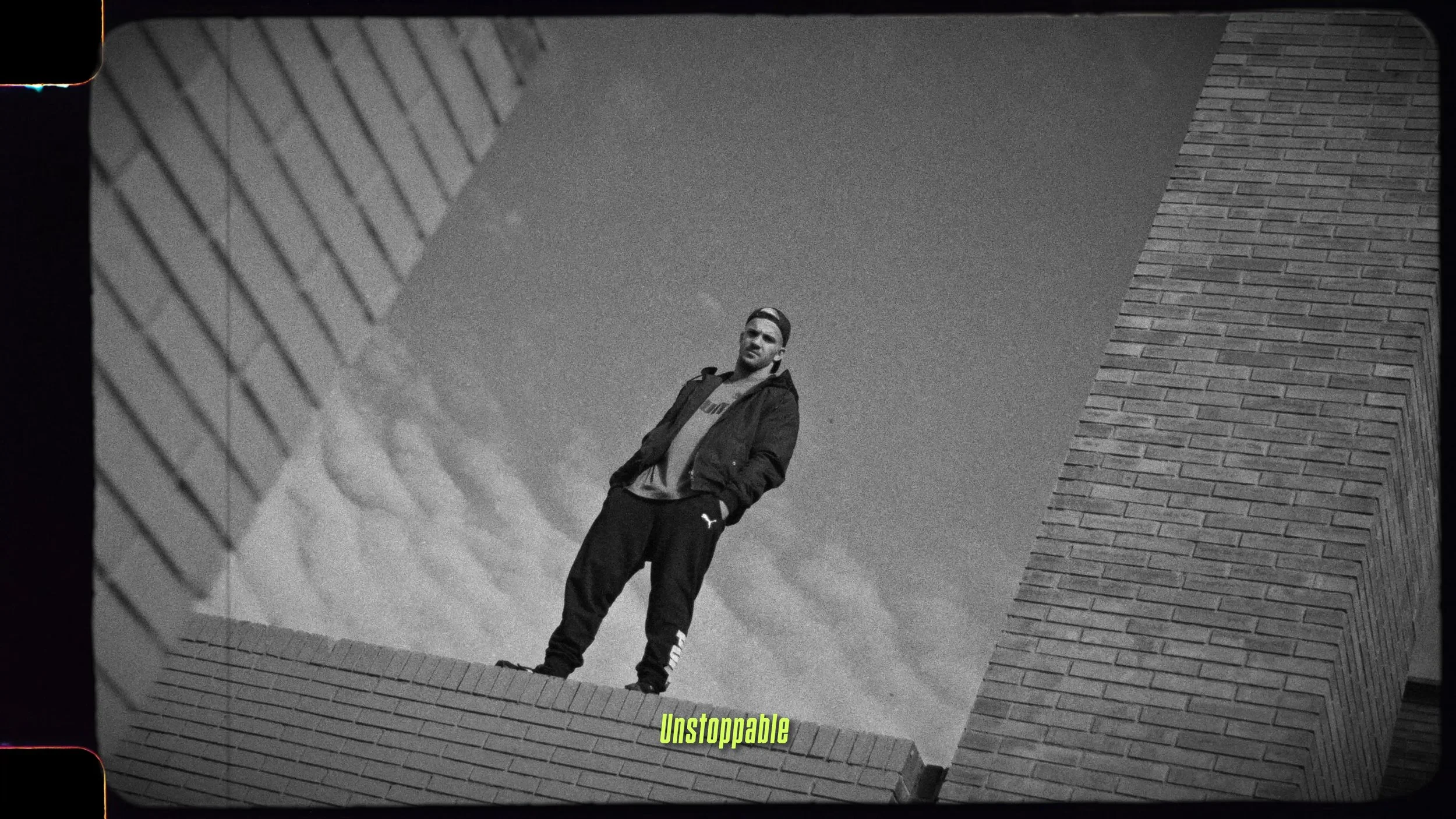 A man standing on a brick ledge, framed by geometric brick walls, looking confidently at the camera with the word "Unstoppable" in bright green text at the bottom.