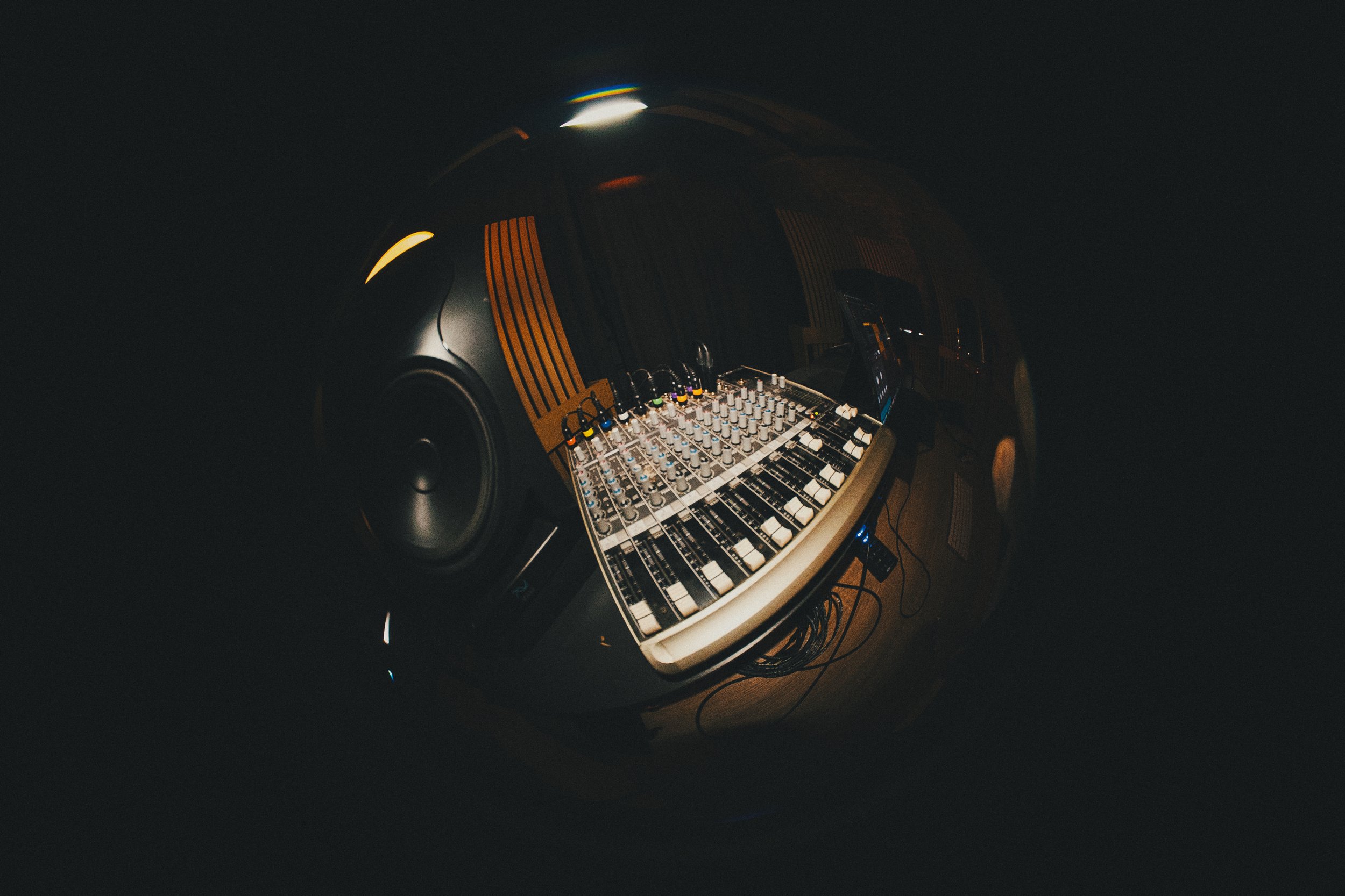 A music mixing console with knobs and sliders in a dark room, reflected in a spherical mirror.