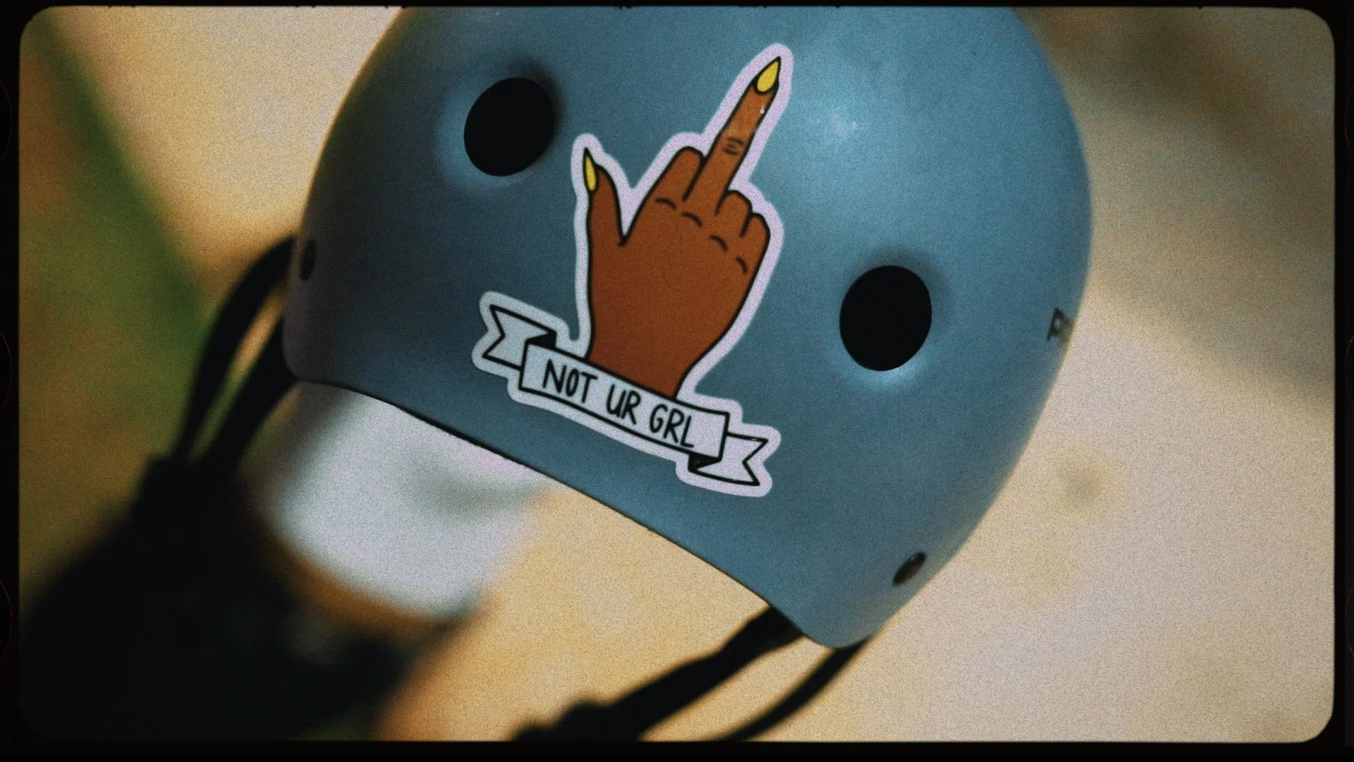 A blue helmet with a sticker of a hand showing the middle finger and a banner that says 'NOT UR GRL'.