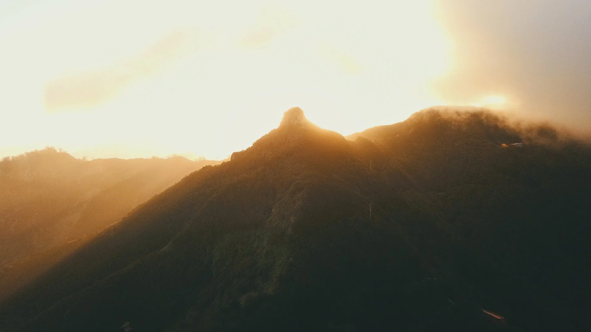 Mountains at sunset with a peak illuminated by the sun, partially covered with mist or fog.