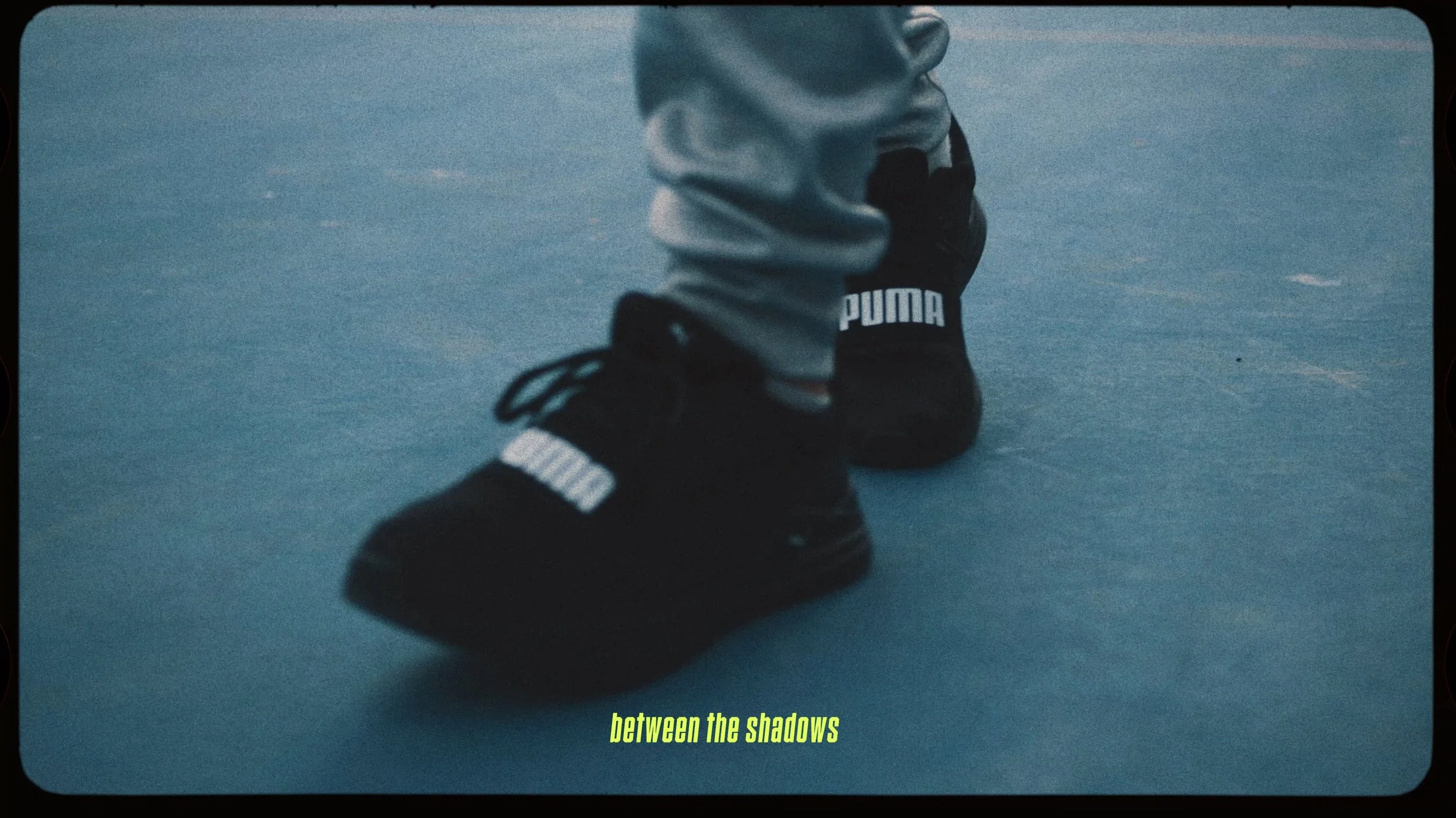 Close-up of a person wearing black Puma sneakers and gray sweatpants, walking on a blue indoor floor.