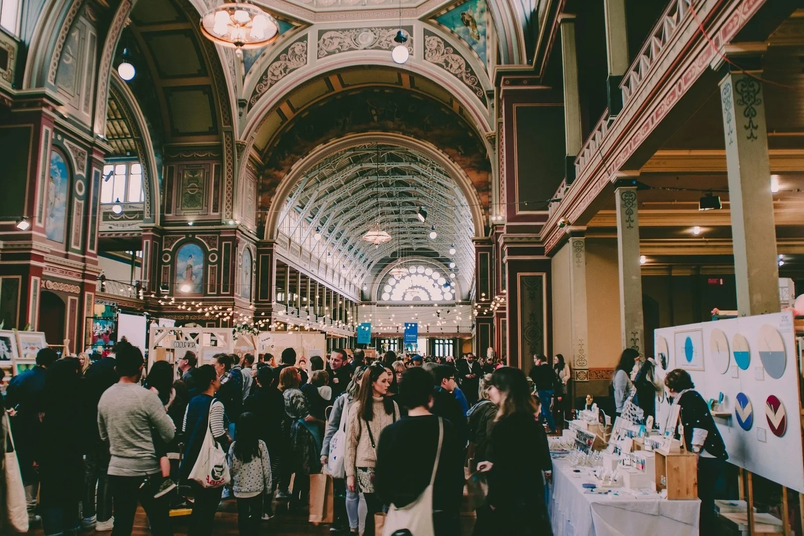 Busy exhibition hall with stalls and visitors under a historic domed ceiling