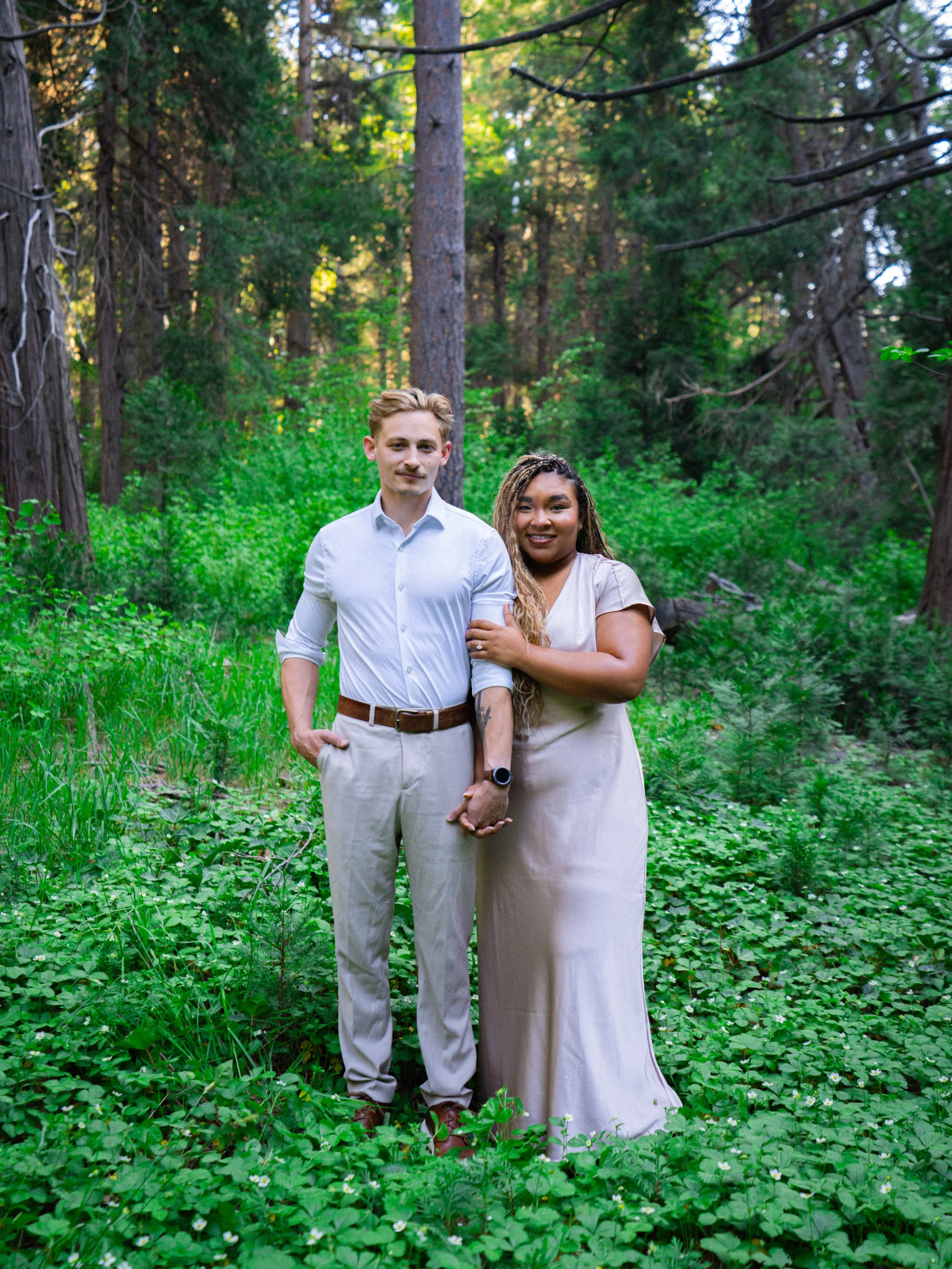 Luxury engagement photographer. A couple poses under the green forest.