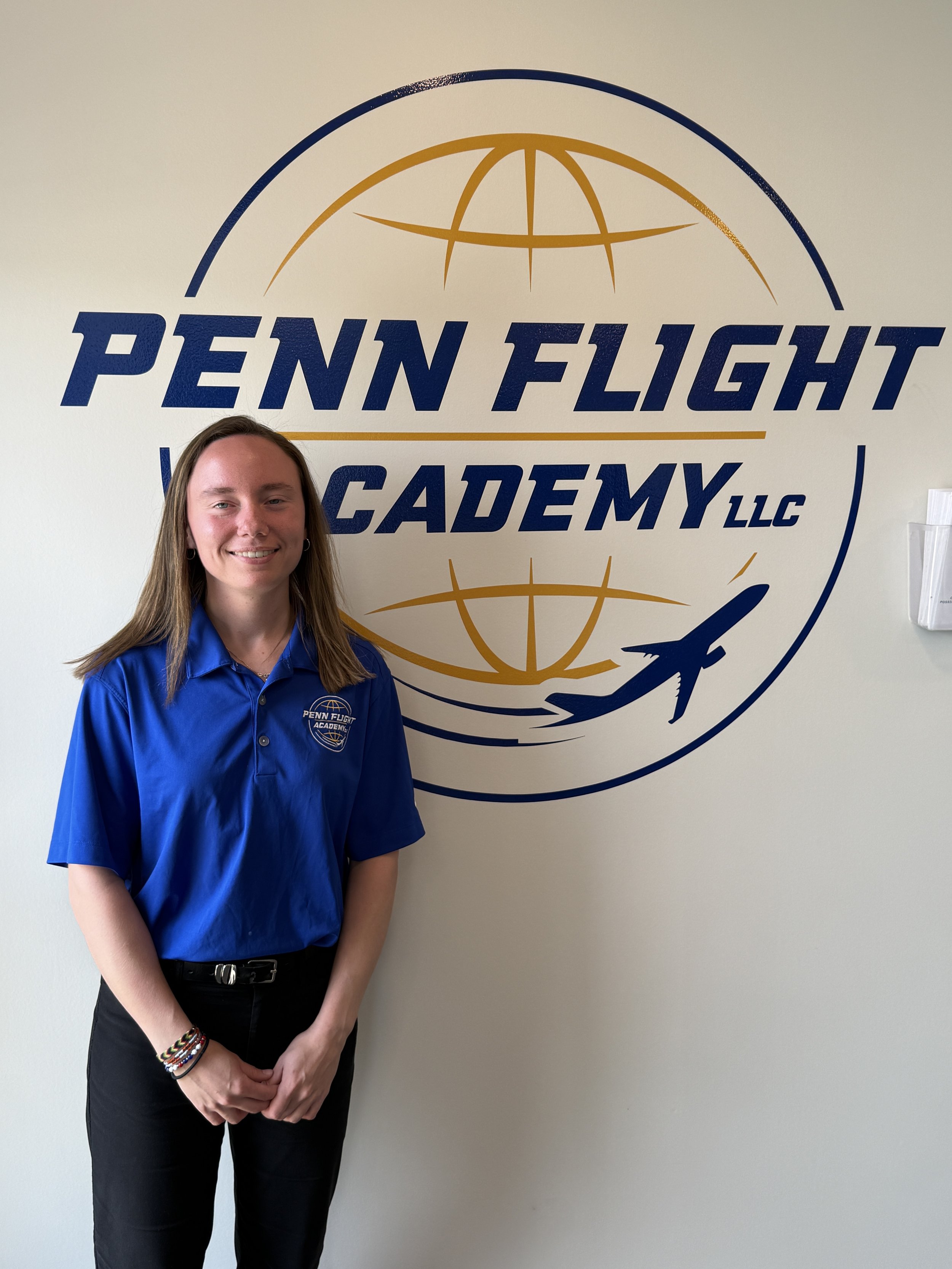 Smiling person wearing a black "Penn Flight School" polo shirt, standing outdoors with sunglasses hanging on the shirt.