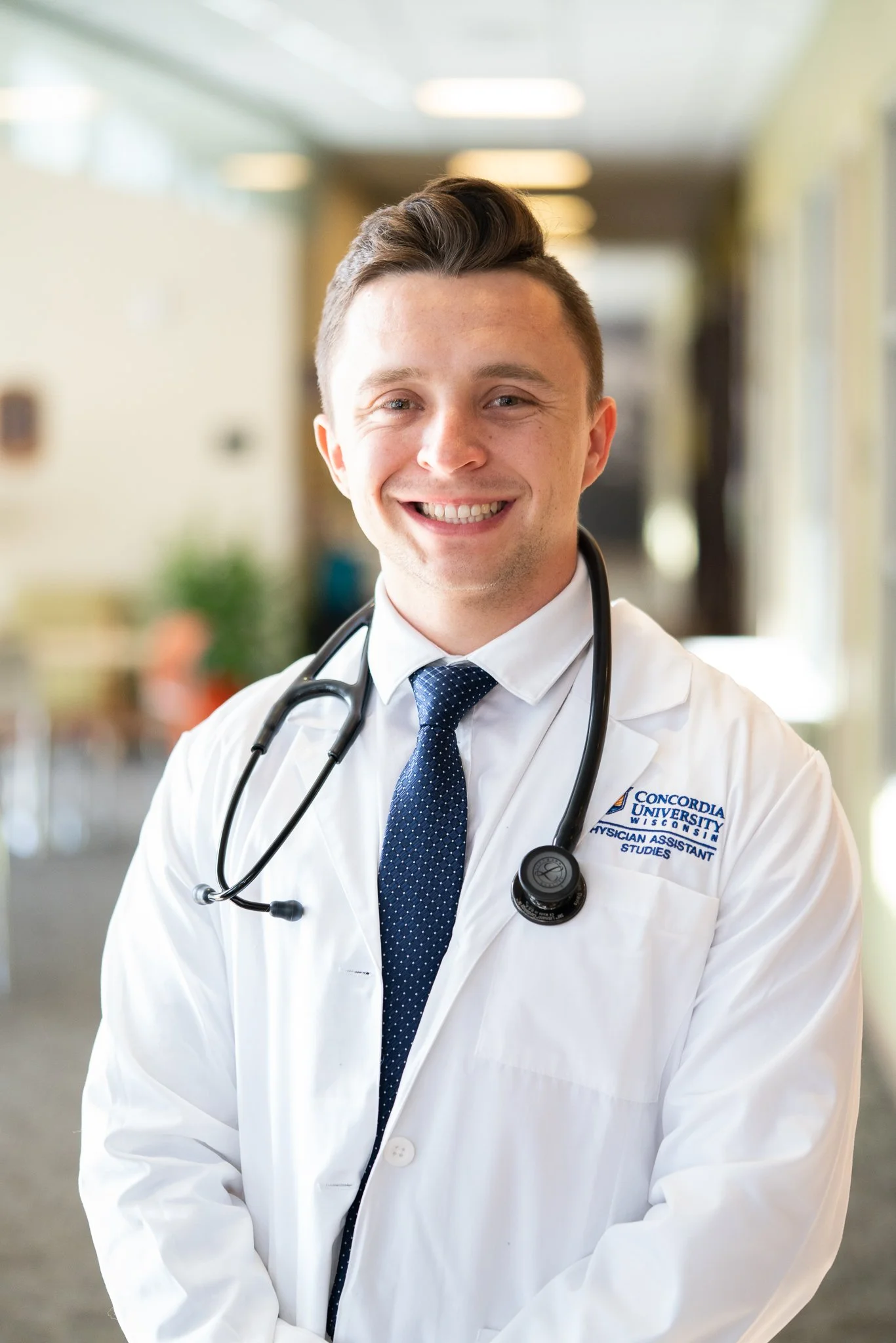 A smiling male doctor standing with arms crossed in a medical office or hospital room.