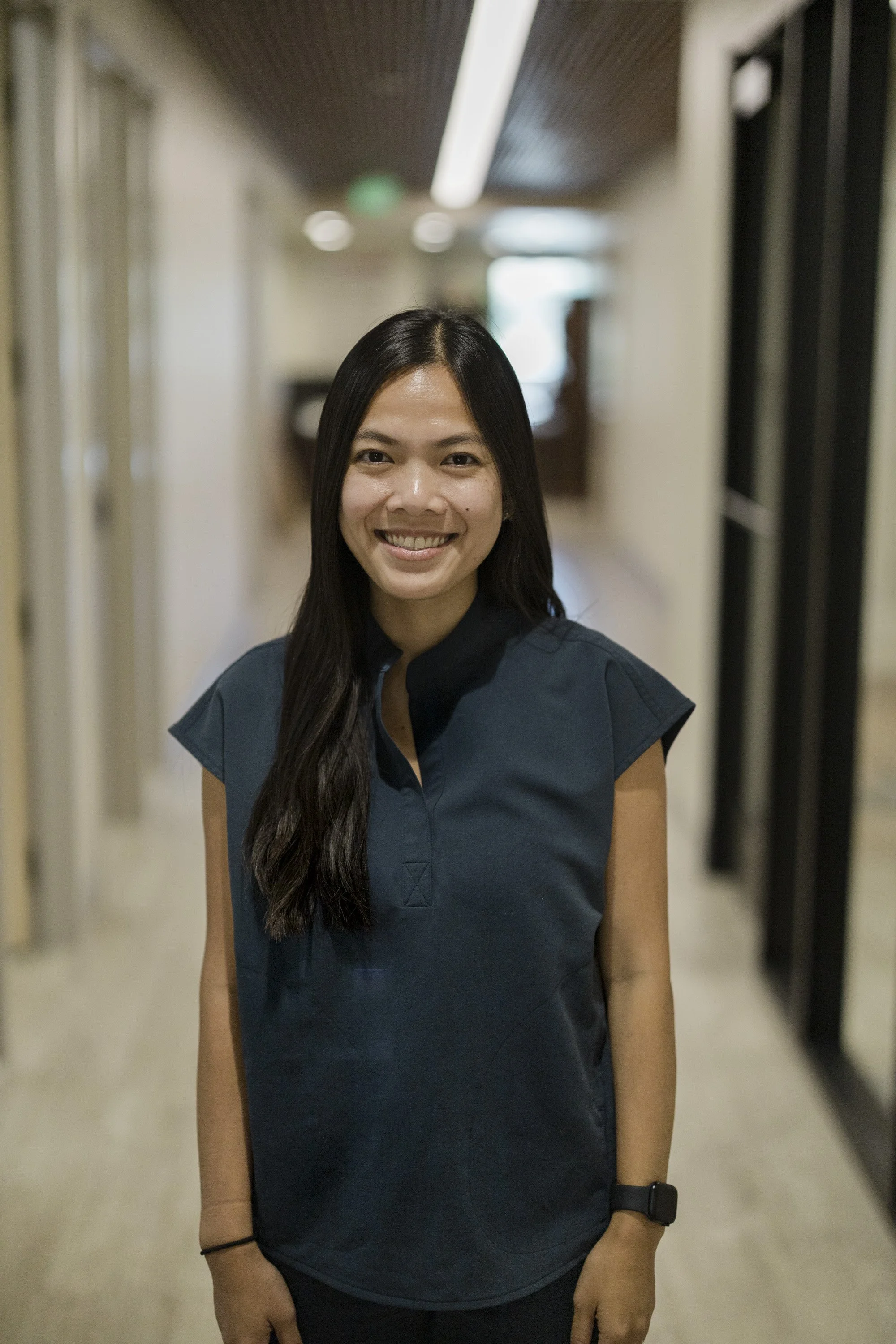 Smiling woman in dental clinic, standing in front of dental chair and equipment.