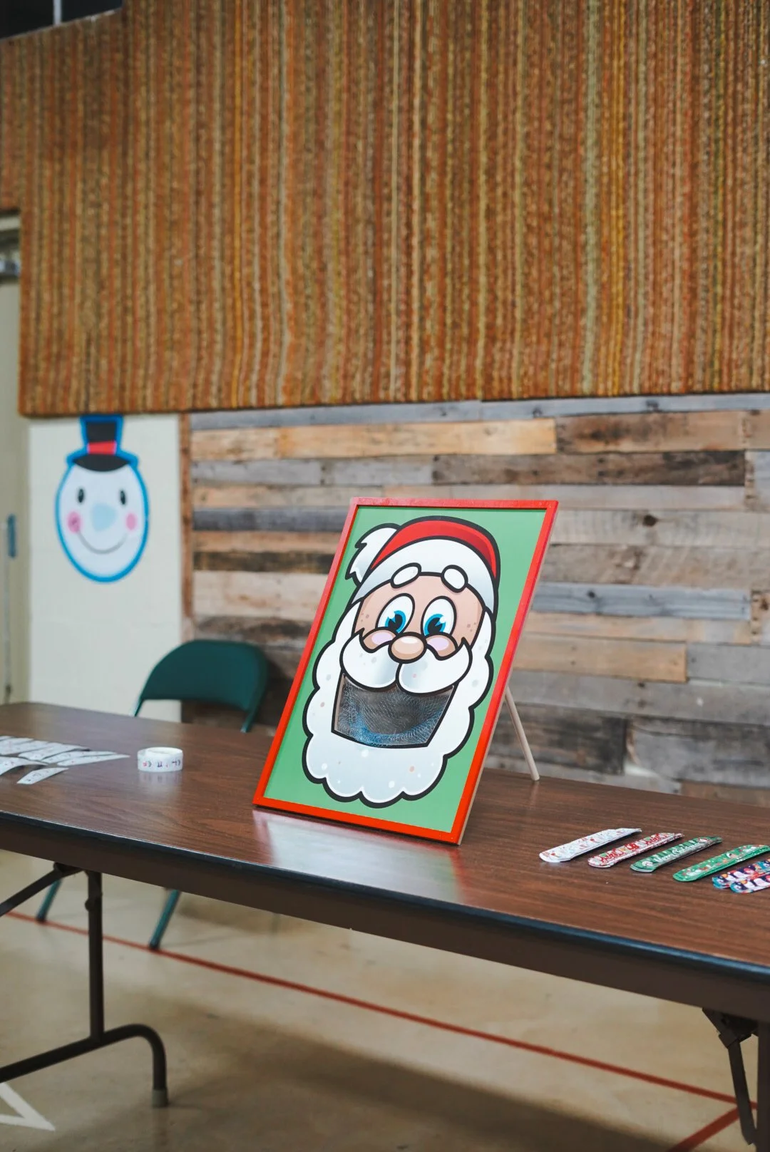 Christmas-themed face mask on display with a Santa Claus illustration on a sign, placed on a table in a decorated room.