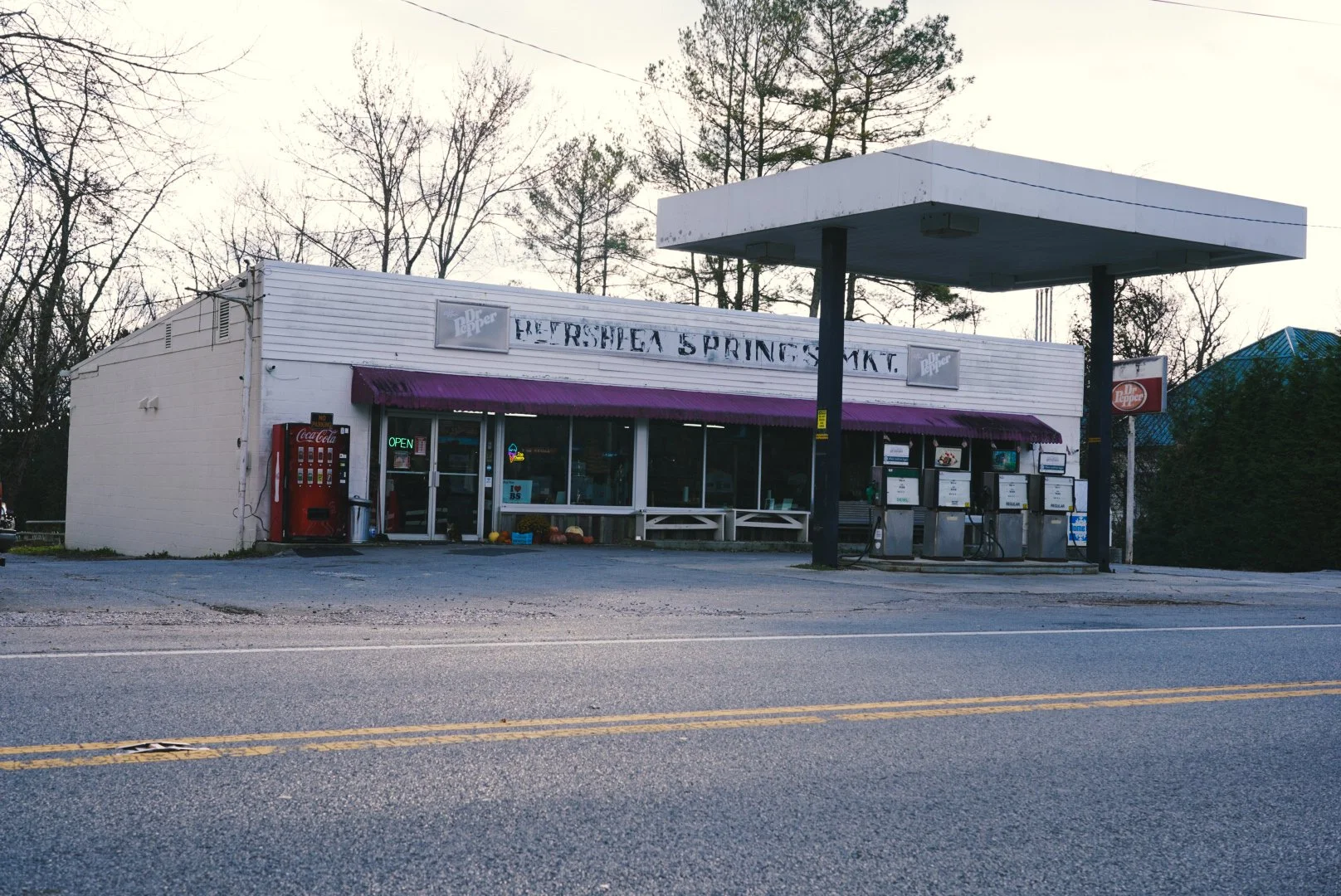 A small convenience store with a purple awning named 'Freshea Springs Mkt.' next to a gas station with four fuel pumps and a large white canopy.