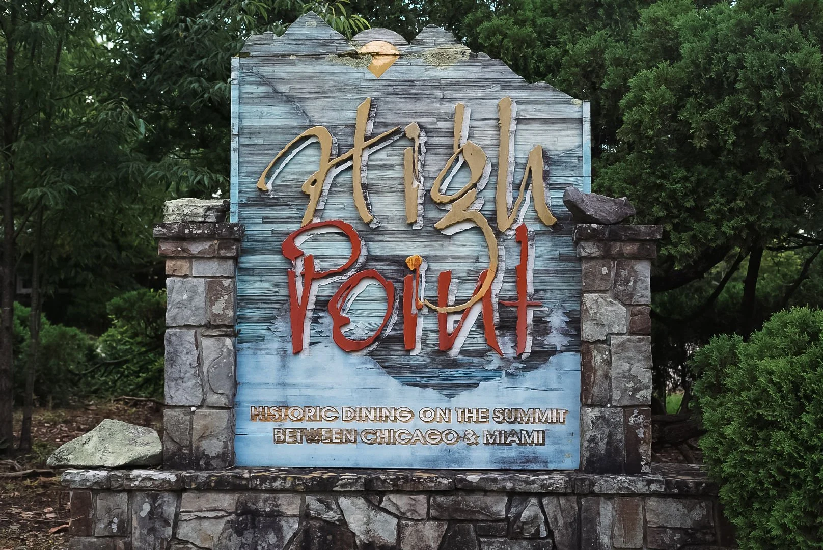 Sign for Apache Pillow, a restaurant offering historic dining on the summit between Chicago and Miami, with a stone base and trees in the background.