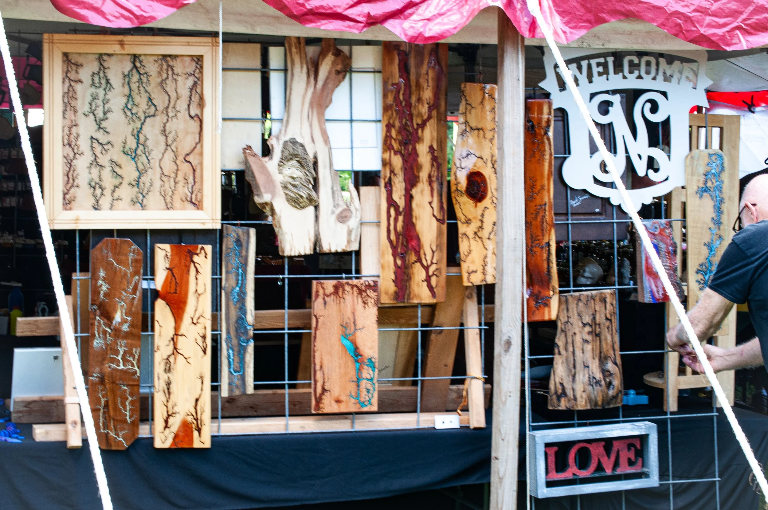 Display of handcrafted wooden art pieces with intricate crackle patterns and a decorative "LOVE" sign at an outdoor market stall.