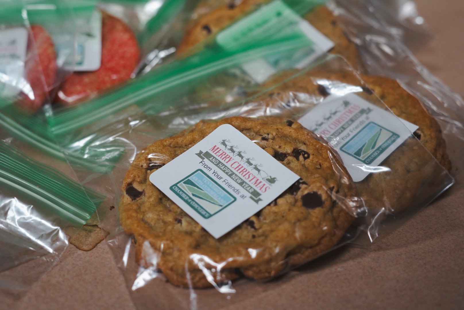 Chocolate chip cookies in plastic bags with Christmas labels that read "Merry Christmas and Happy New Year from your friends at Challenger.