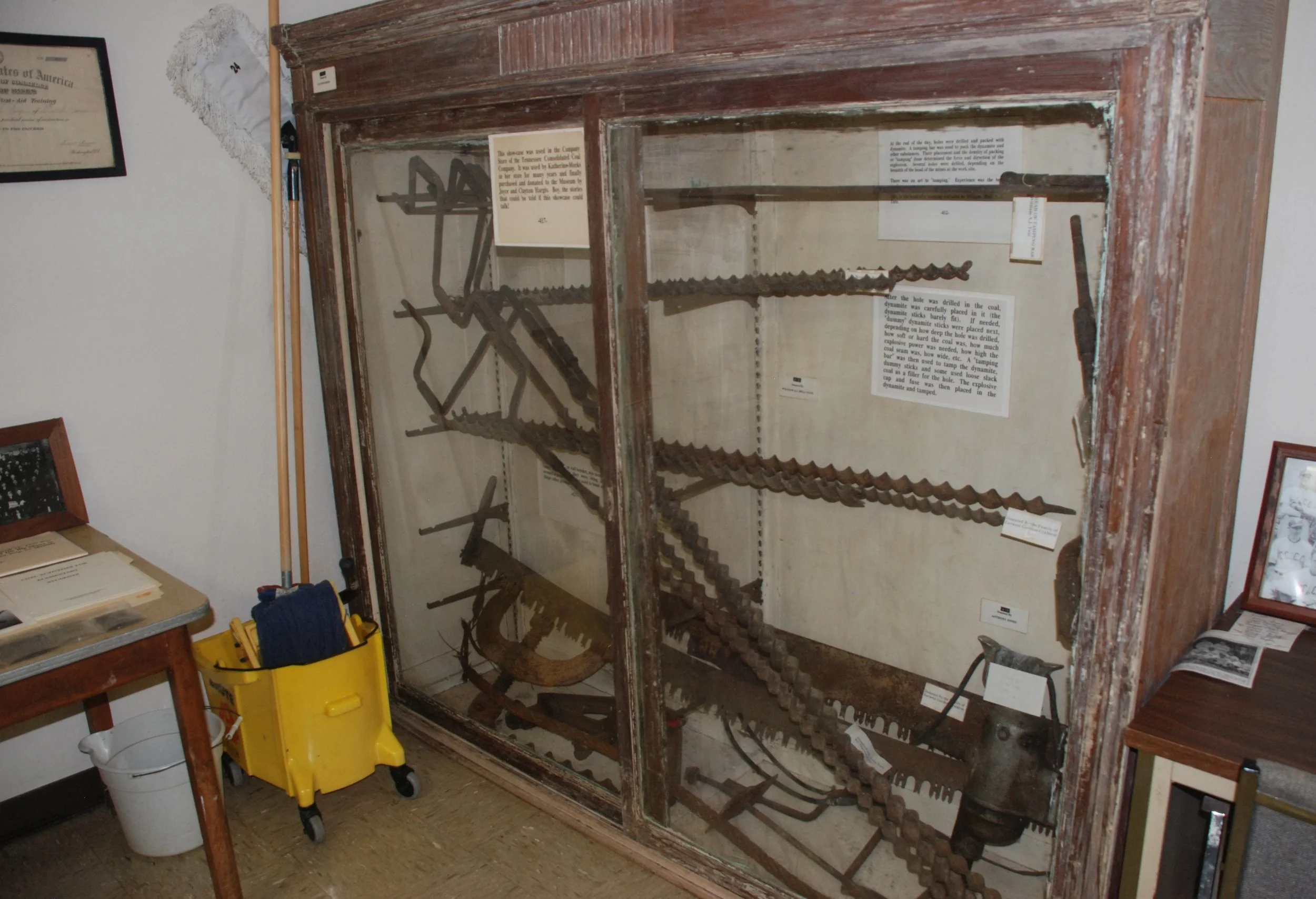 A display case with antique saws and tools, along with informational plaques, inside a museum or historical exhibit.