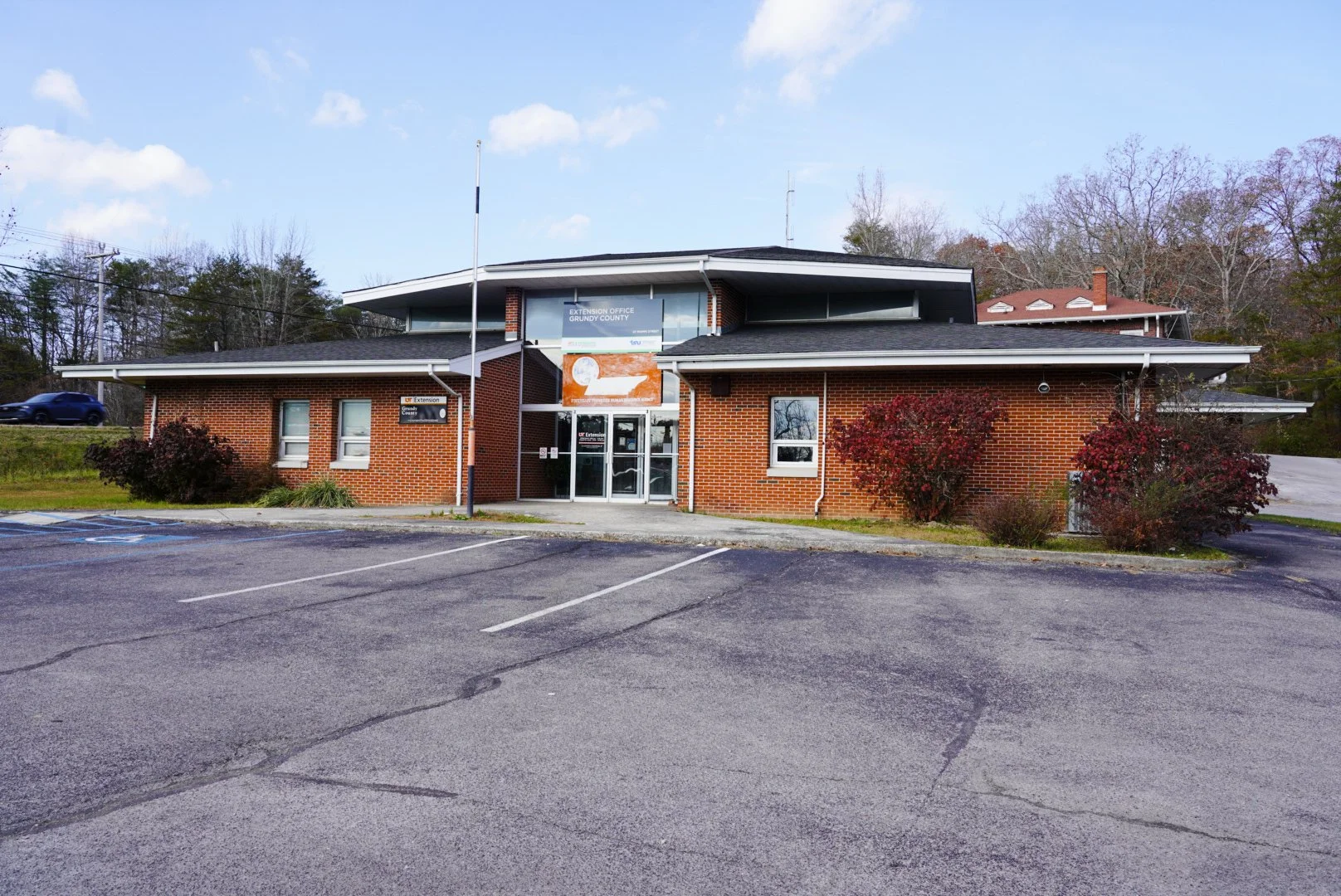 Brick building with glass entrance, signage indicating it is the Extension Office for Grundy County, surrounded by parking lot with a few vehicles and trees in the background.