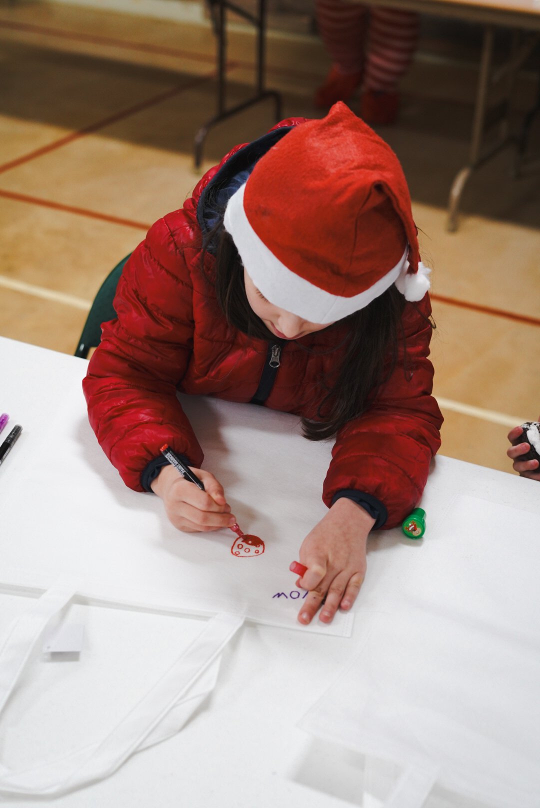 Person wearing a Santa hat and red jacket drawing on paper at a table.
