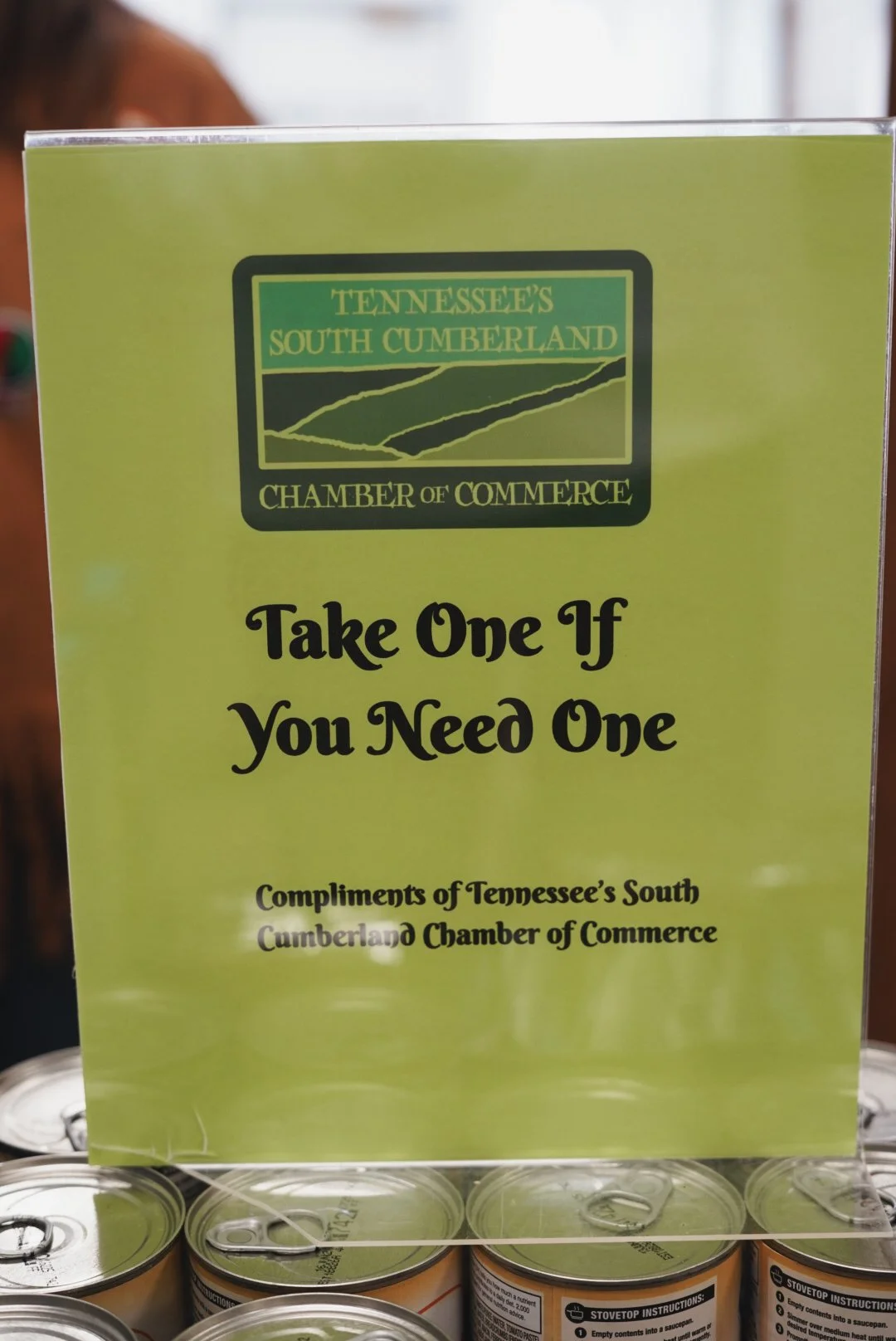 Sign from the Tennessee's South Cumberland Chamber of Commerce that says, 'Take One If You Need One,' with cans of food underneath.