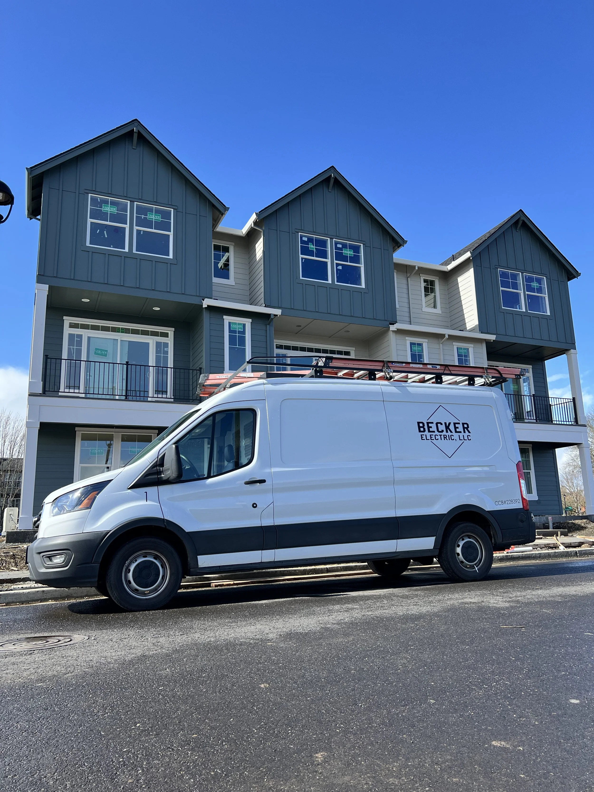 A white van labeled 'Becker Electric, LLC' parked in front of a modern multi-story residential building under construction.
