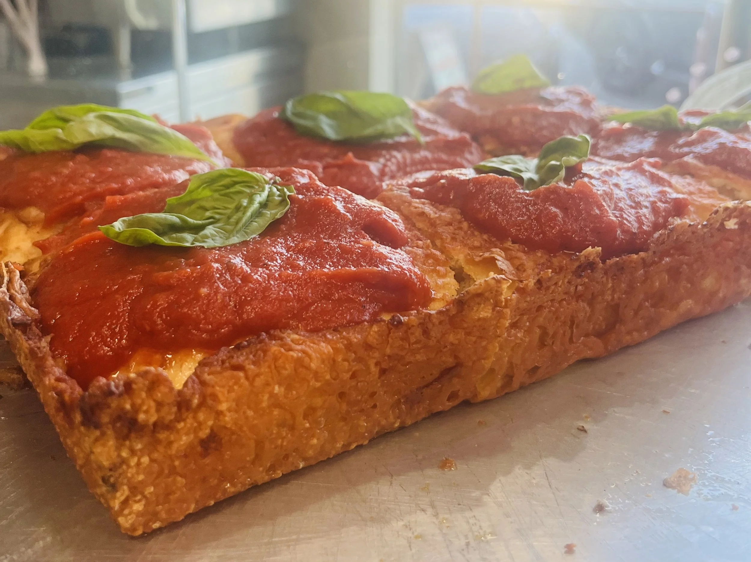 Detroit style pizza with the cheesy crust and basil on top. 