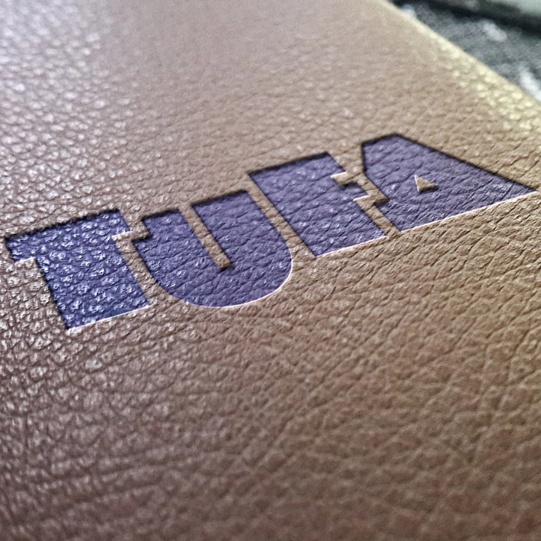 Nahaufnahme eines Papiers mit eingedrucktem, blauer Buchstaben 'TUIA' auf sandfarbener Oberfläche.