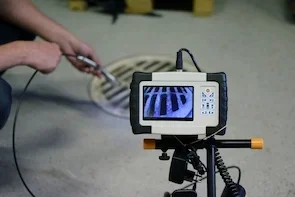 A pipe inspection camera viewing a sewer drain opening on a concrete floor.