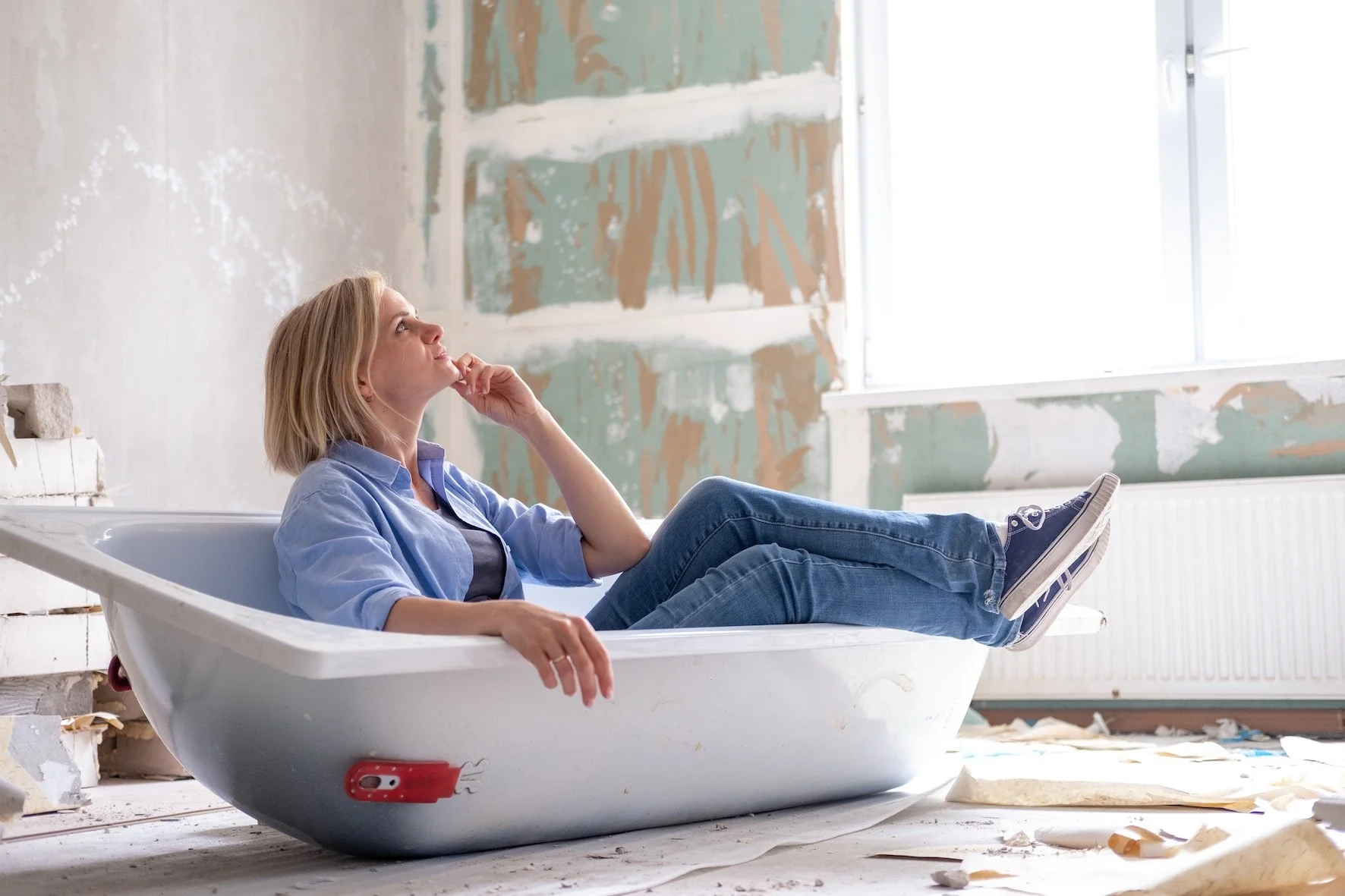 Woman sits in uninstalled bathtub and plans her bathroom renovation