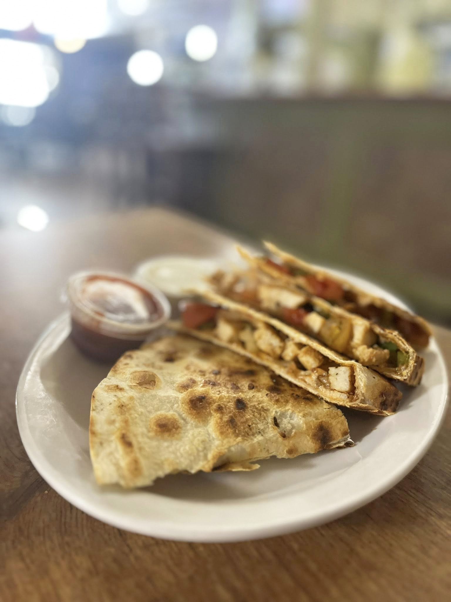 A plate with a quesadilla, a folded taco, and a small container of salsa on a wooden table.