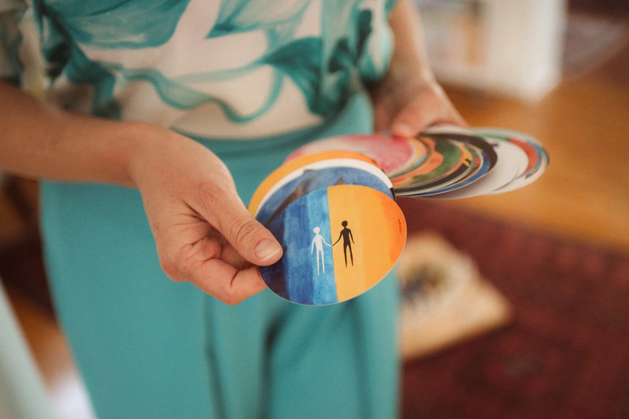 A person holding a circular sticker with design of a rainbow and two people holding hands, one white and one black.