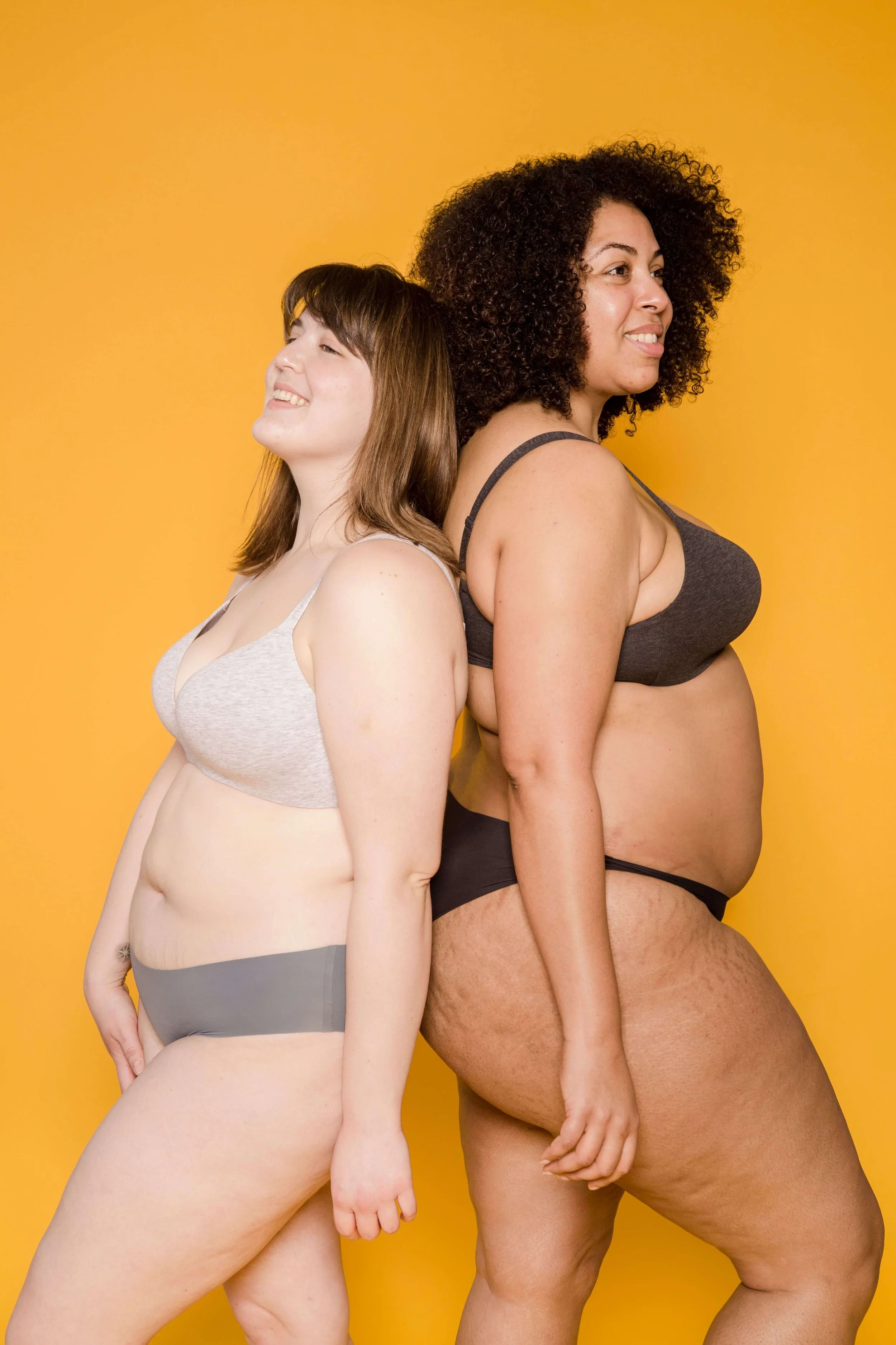 Two women of different body types stand back to back, smiling confidently. Are you caught in the summer body trap, tying your worth and enjoyment to how your body looks? Emotional regulation therapy in Davie, FL, can help.