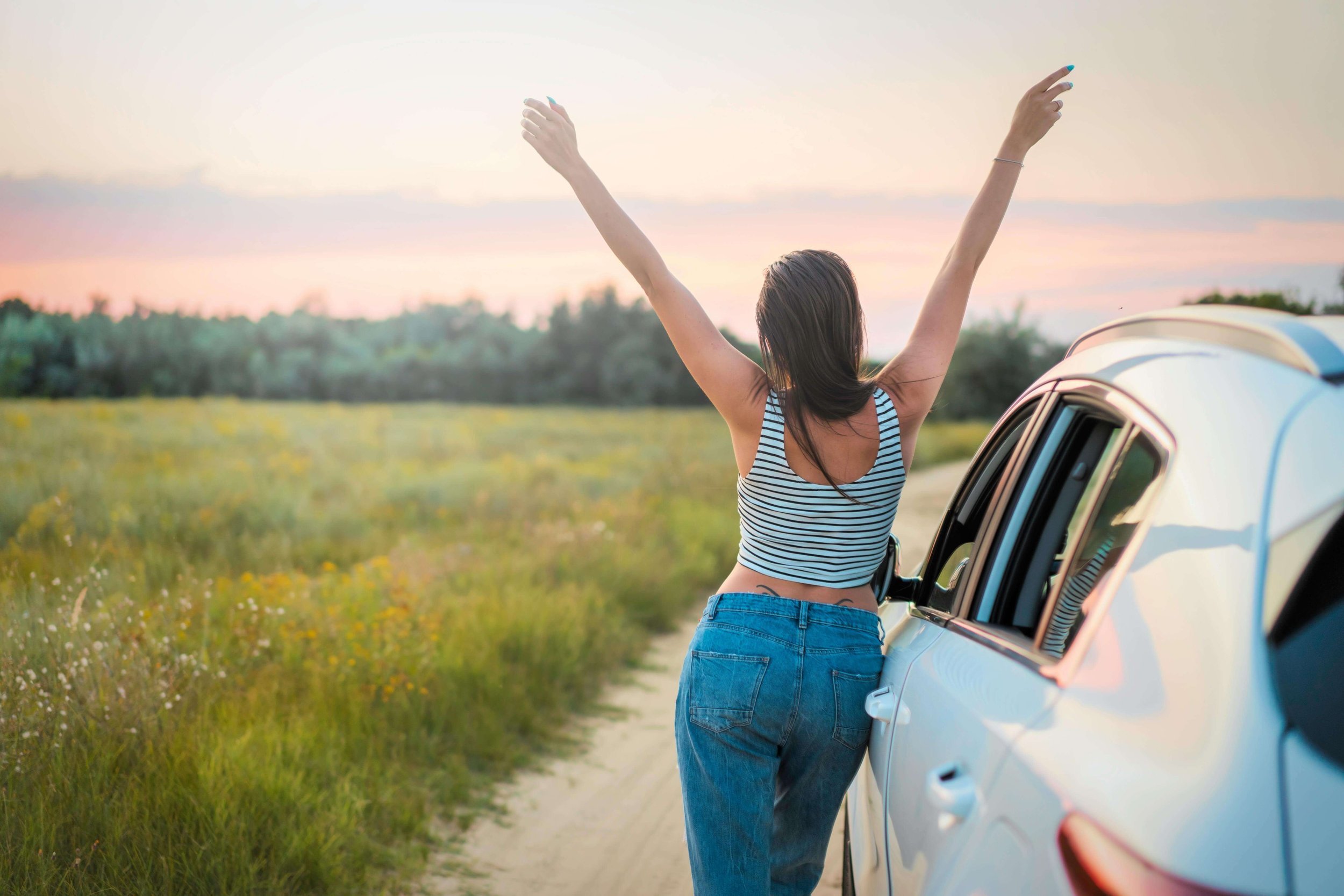 A woman stands beside a car on an open road, arms raised freely toward a sunset sky. Are you outgrowing relationships that no longer align with who you're becoming? Discover compassionate guidance from a relationship therapist in Davie, FL.