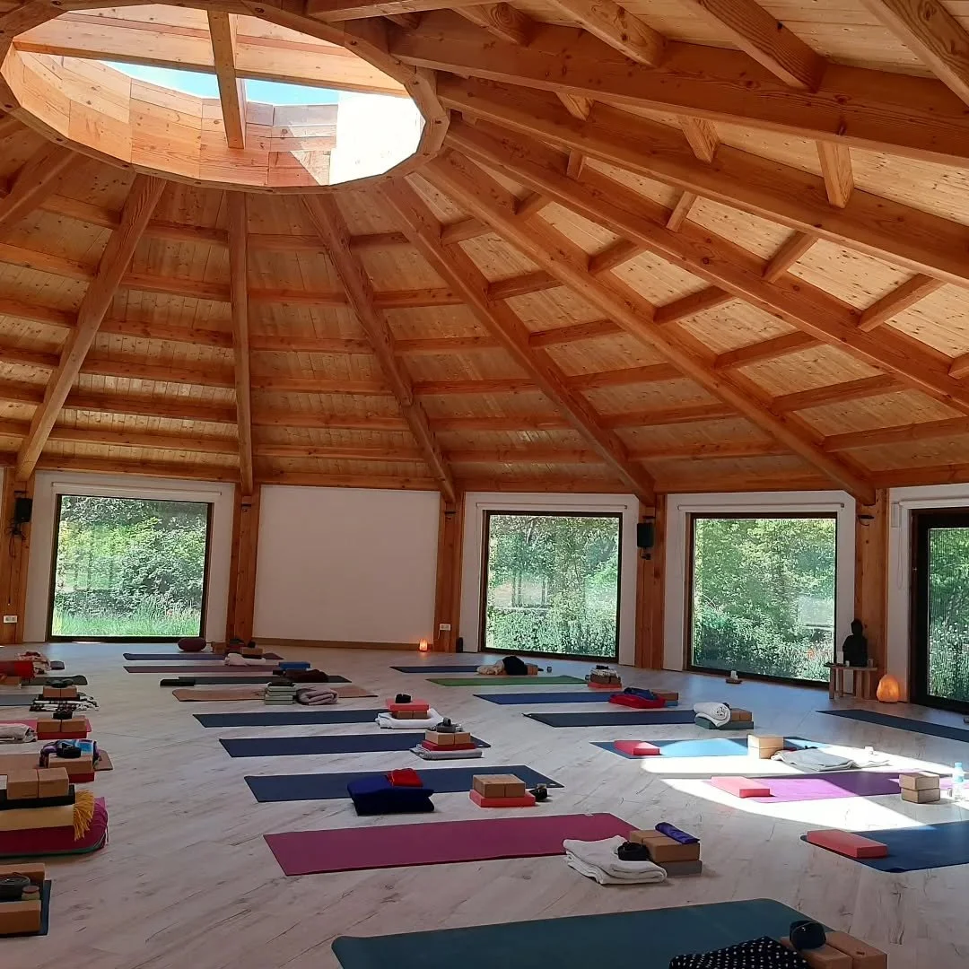 Interior of a yoga or meditation studio with wooden ceiling, large windows, and yoga mats with props arranged on the floor.