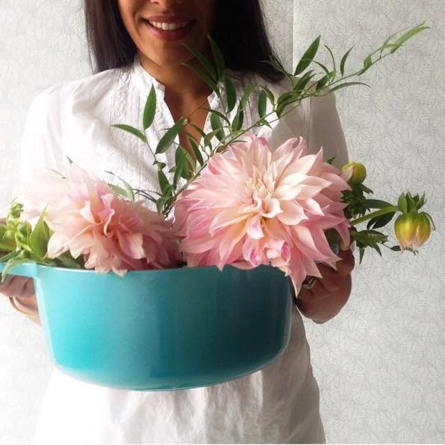 Madhu Puri holding Le Creuset signature enamel cast iron in Caribbean filled with blooming dahlias.