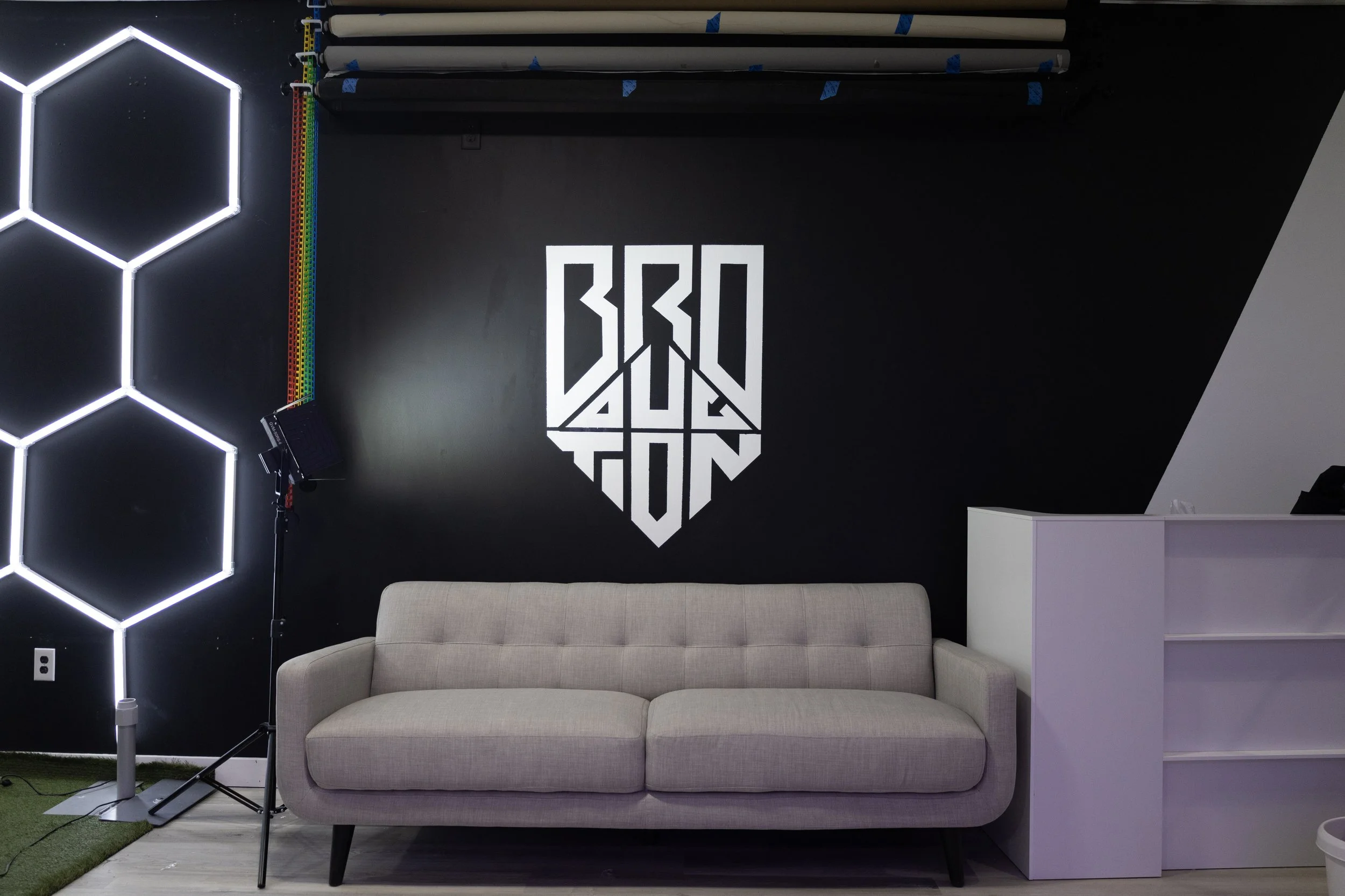 Black and white portrait of a blonde woman holding a Canon camera, looking directly at the camera with a serious expression, against a dark background.