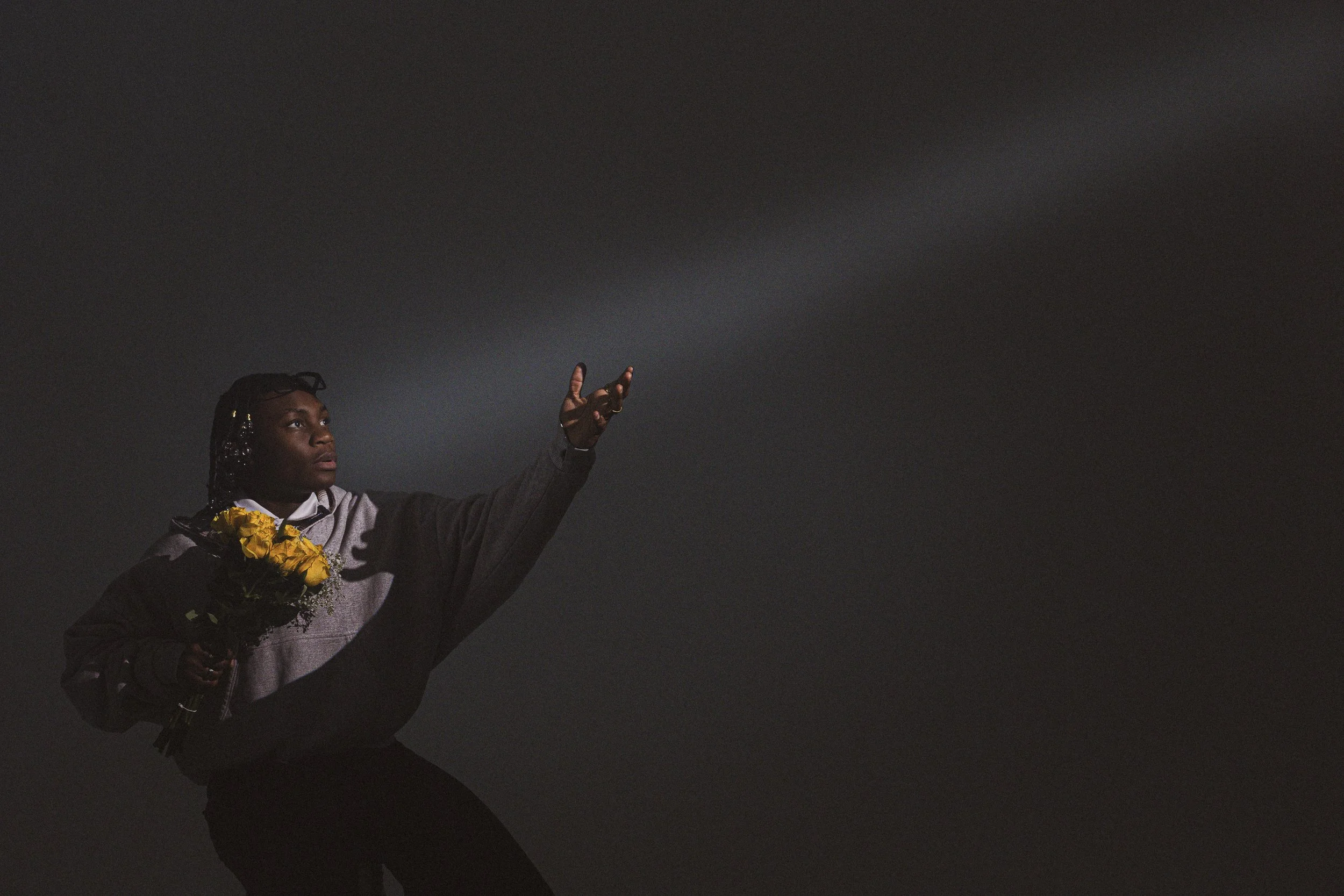 A person with braids and glasses holding a bouquet of yellow flowers, extending their arm towards a dark, starry sky.