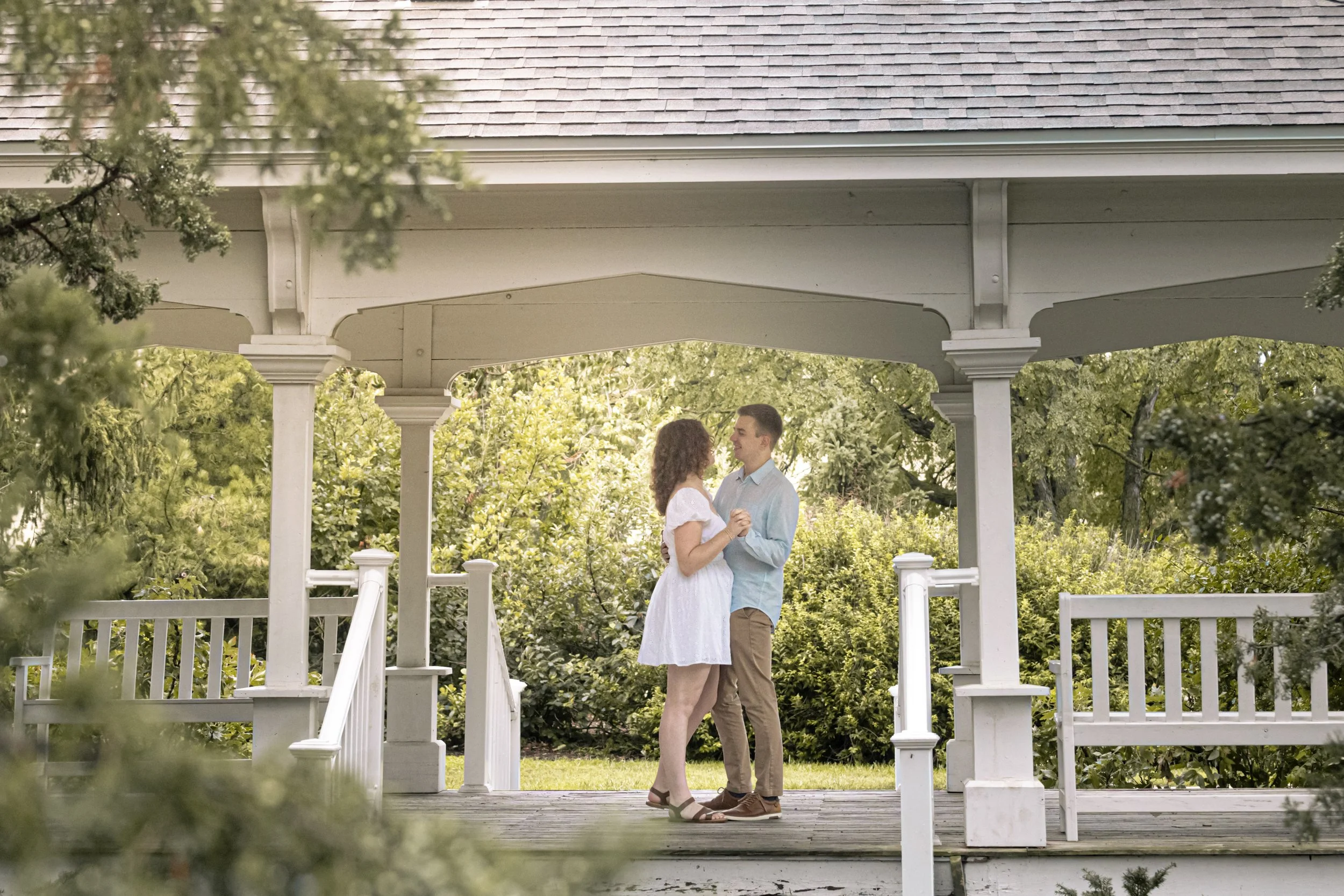 A couple dancing on a gazebo surrounded by greenery in a park during daytime.