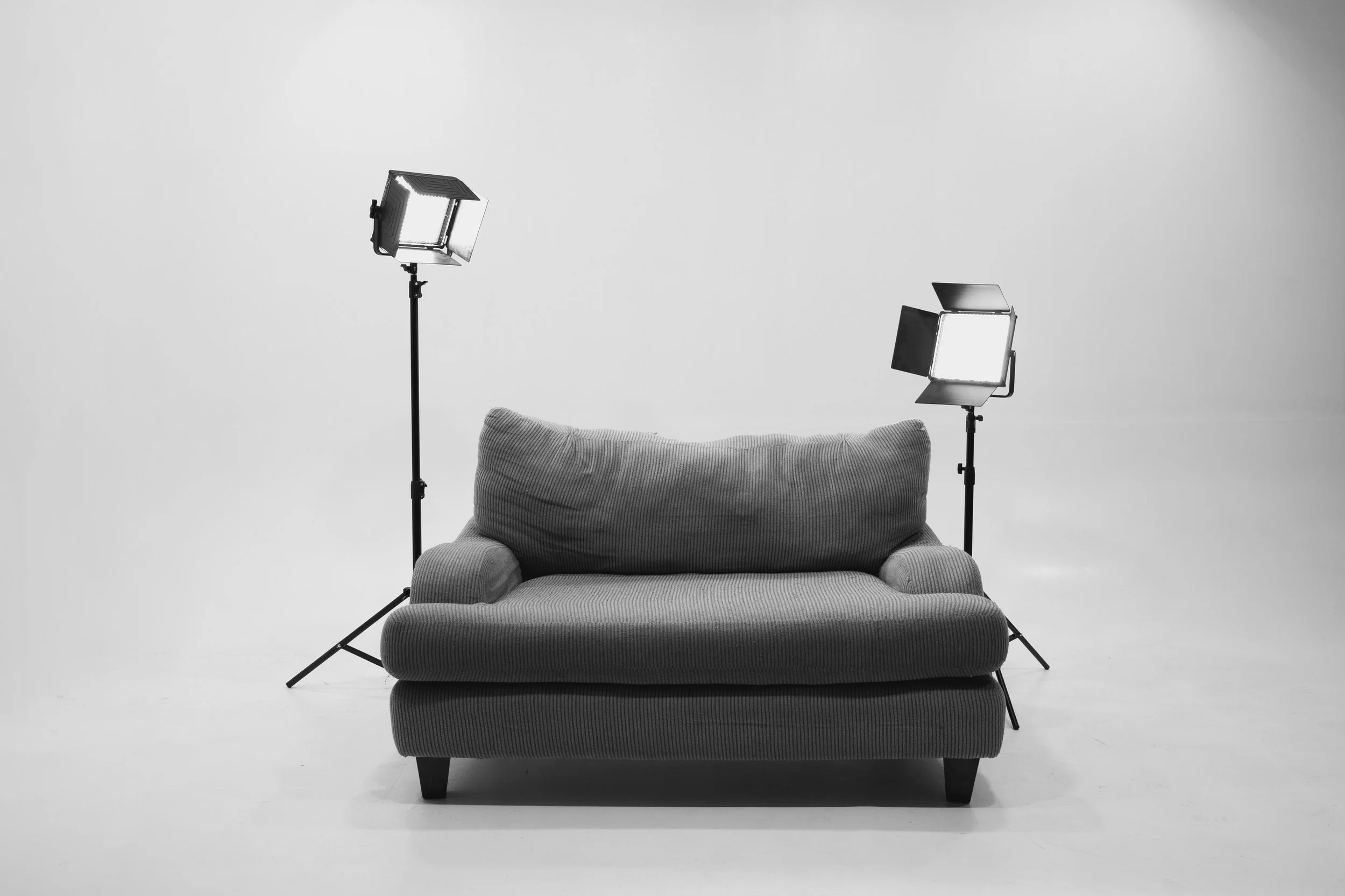 Black-and-white portrait of a young man in a suit holding a Canon DSLR camera, looking directly at the camera.