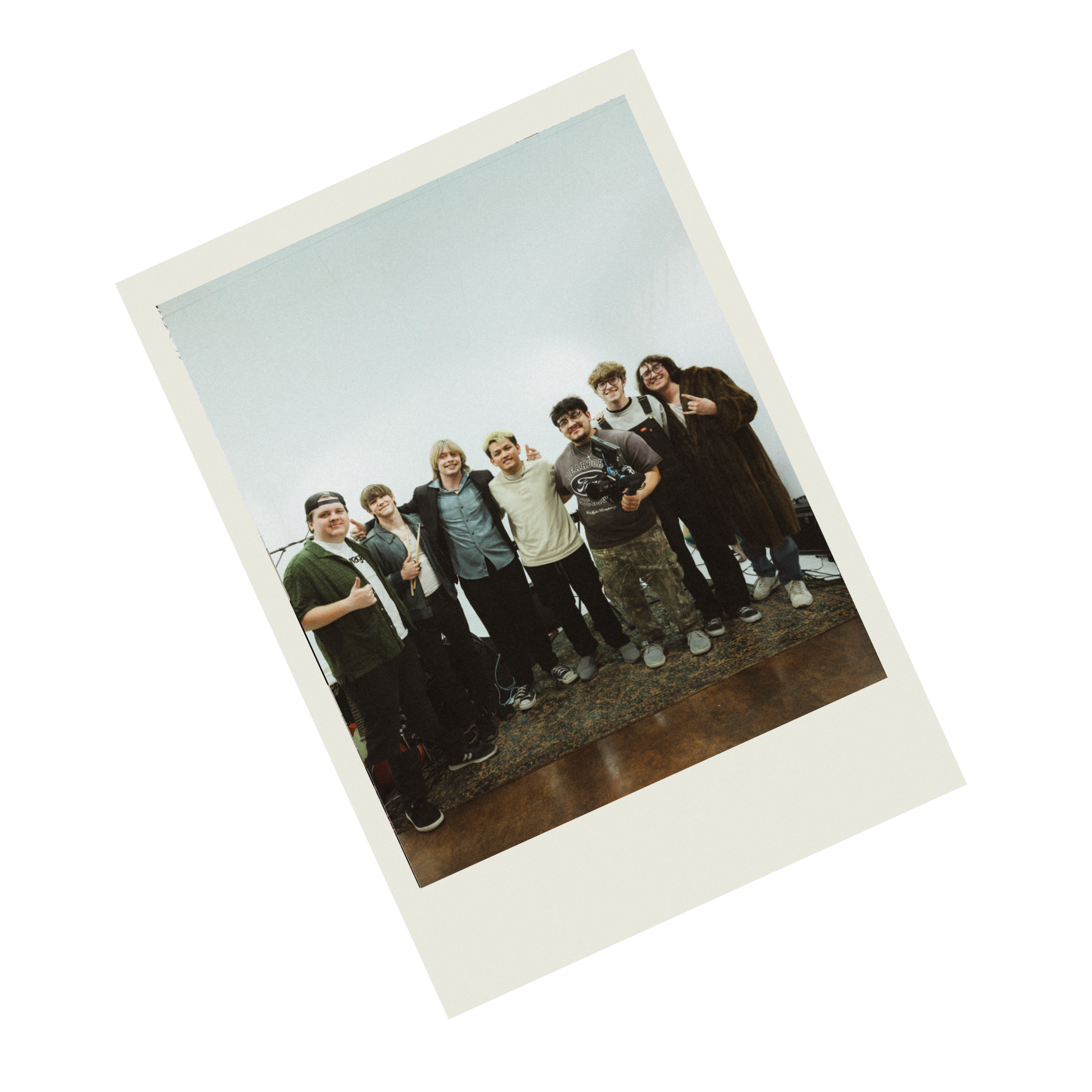 A group of people, smiling and posing together, standing inside a room with an overcast sky visible through a window behind them.