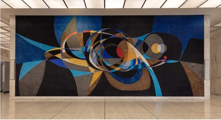 Seymour Fogel mural. Abstract geometric mural with swirls, circles, and angular shapes in black, blue, gold, red, and white in an indoor setting.