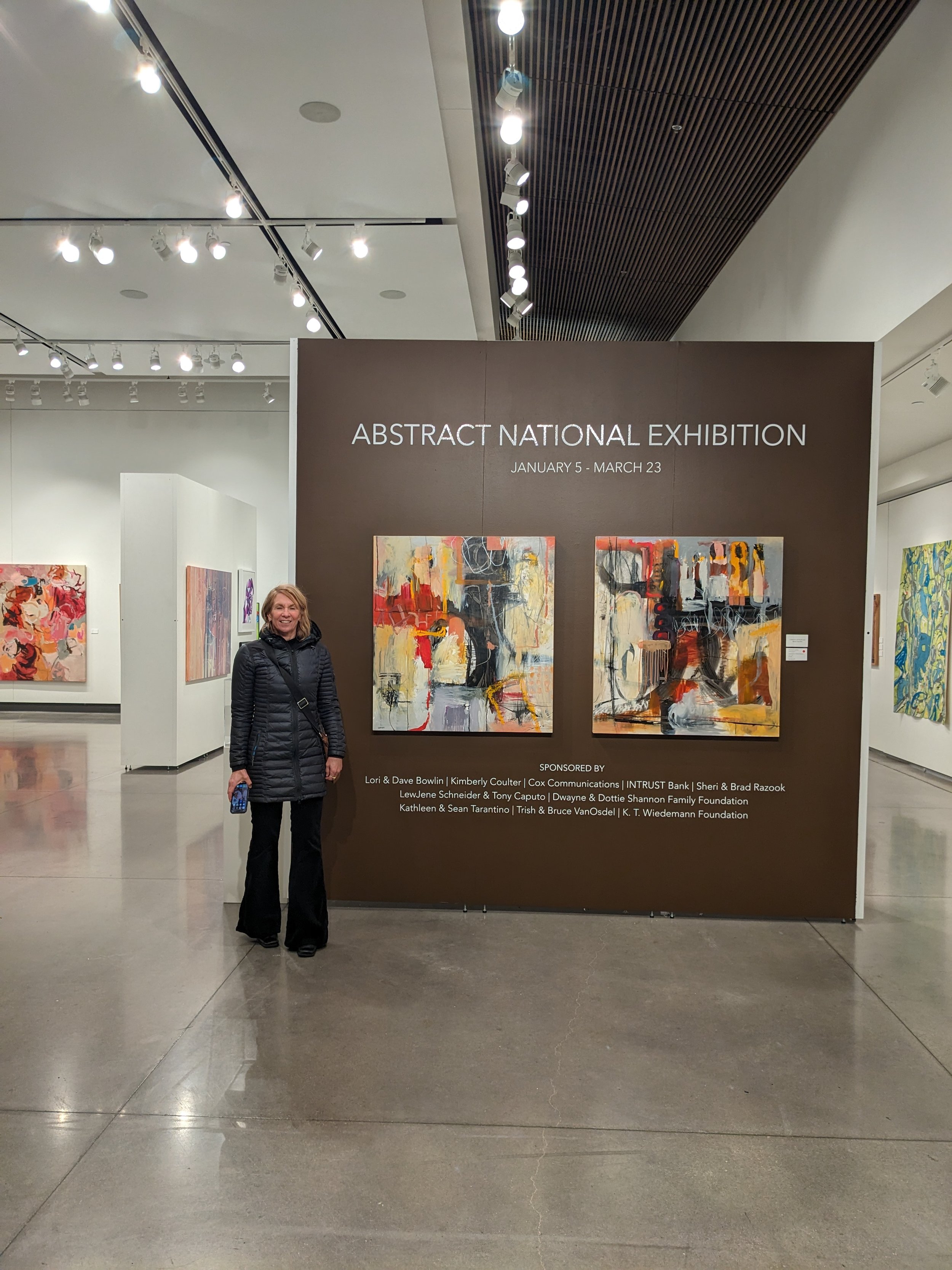 Christine at the 2024 Mark Arts Abstract National Exhibition, which features paintings with abstract designs and vibrant colors.