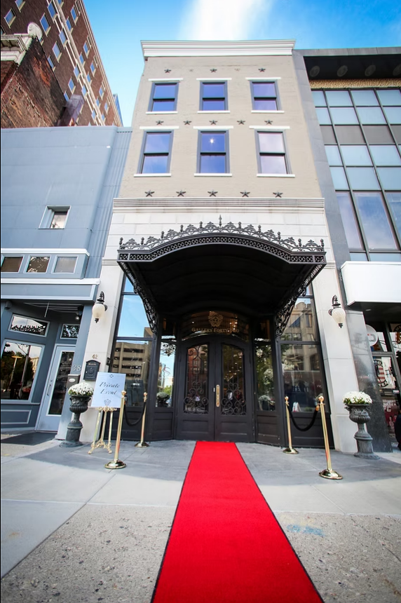 Elegant building with a red carpet leading to a black entrance canopy, surrounded by decorative planters and street lamps.