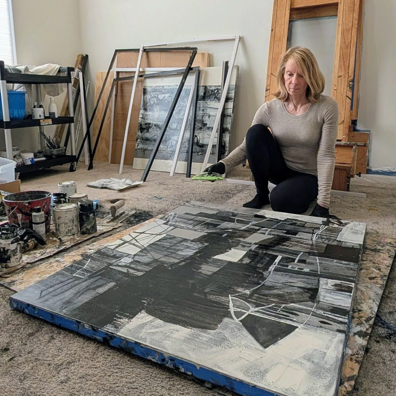 Christine creating a black and white abstract artwork on a large canvas in an art studio with art supplies and framed pictures on the wall.