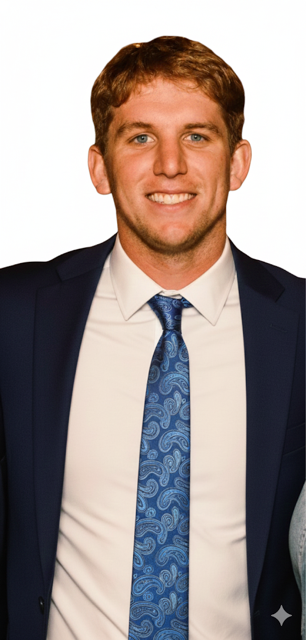 A young man with light brown hair, blue eyes, and a light complexion, wearing a dark suit, white dress shirt, and a blue patterned tie, smiling at the camera against a white background.