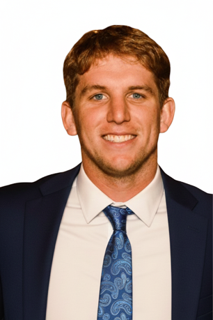 A young man with light brown hair, blue eyes, wearing a dark suit, white shirt, and a blue patterned tie, smiling against a white background.