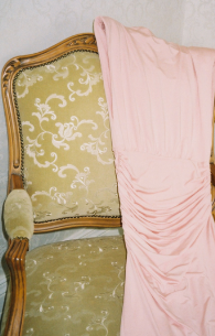 Sofá vintage con tela dorada y un vestido rosa colgado en la esquina.