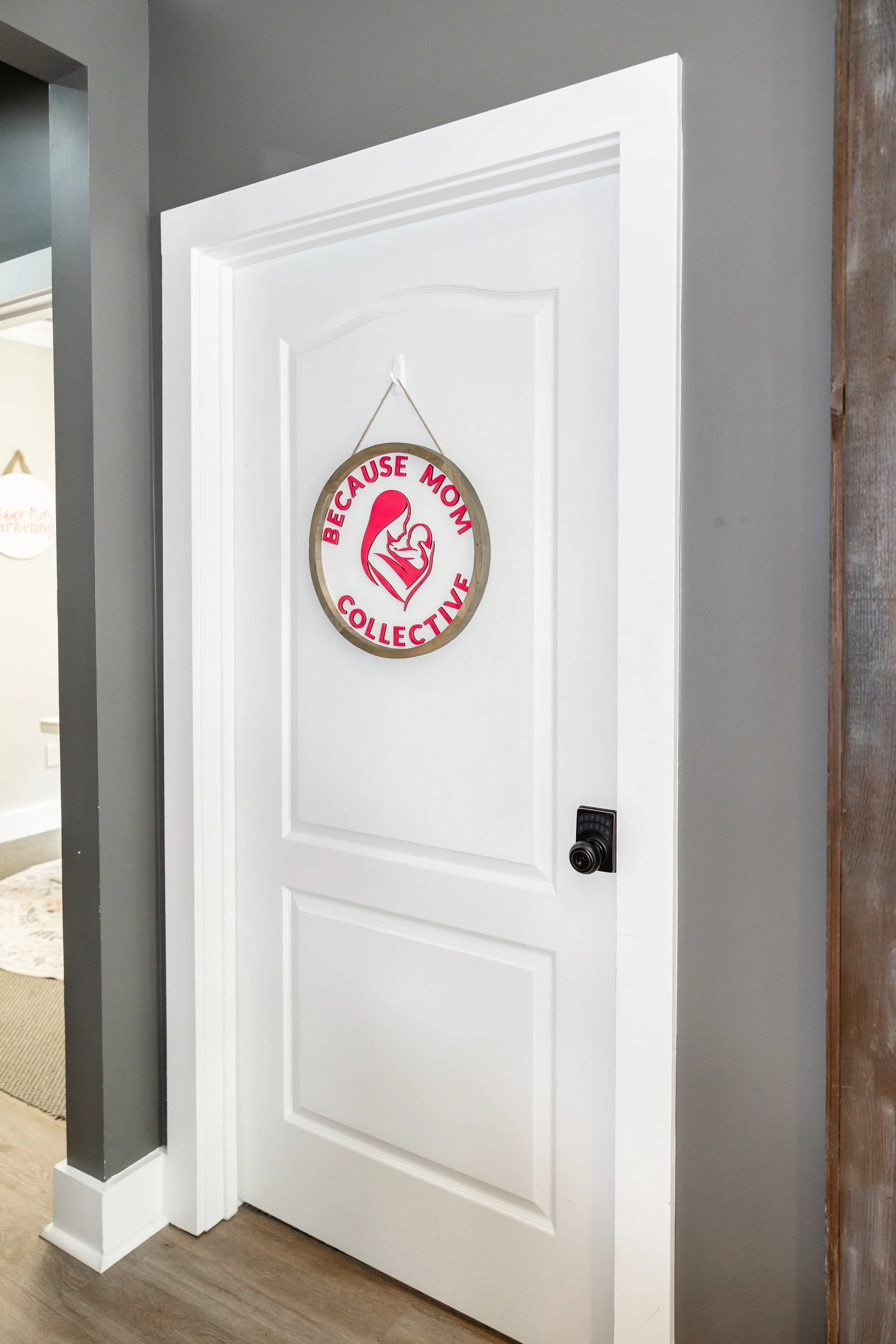 White door with a circular Because Mom Collective sign hanging on it