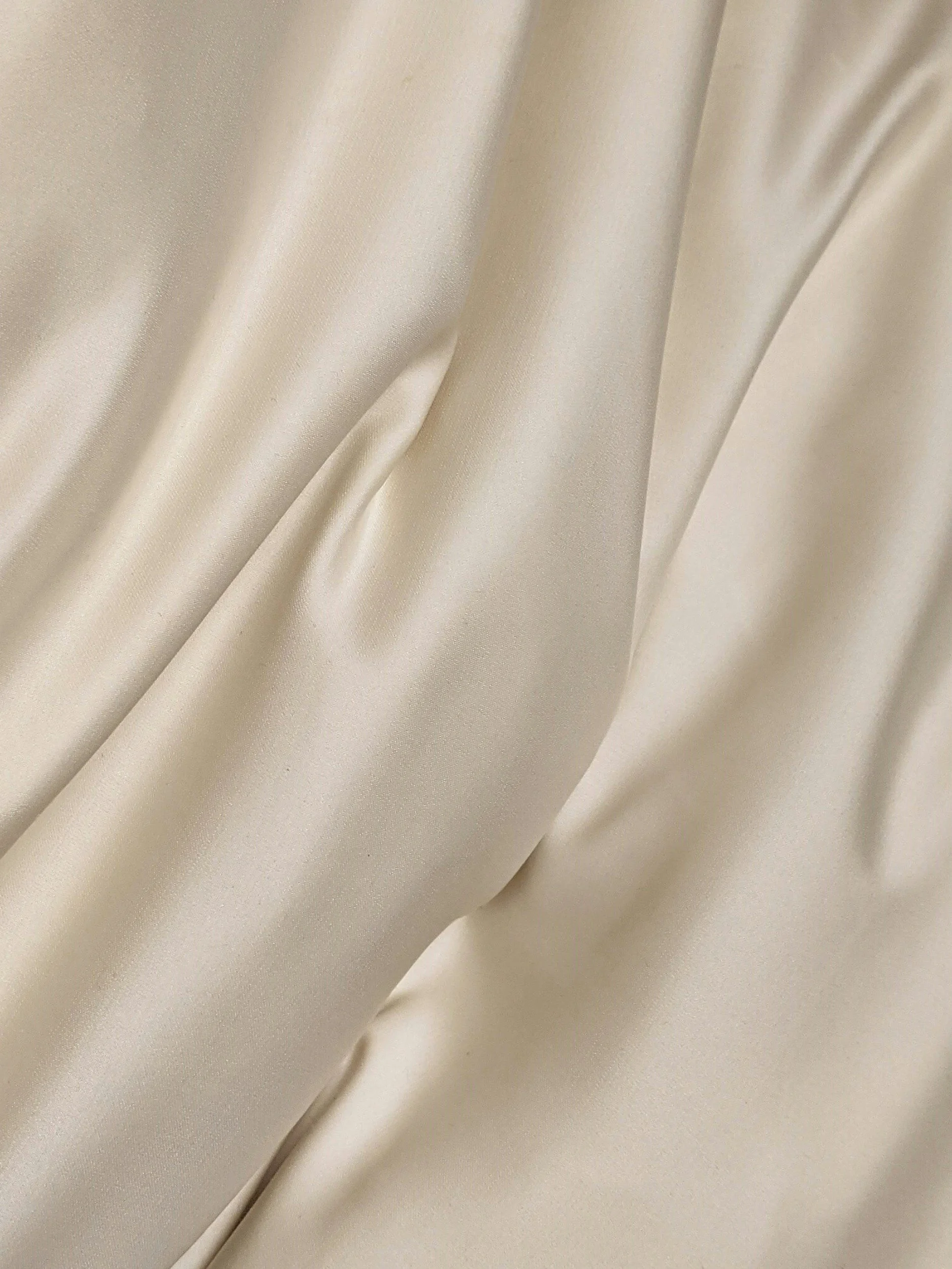 Close-up of cream-colored satin fabric with a smooth, shiny texture and soft folds.
