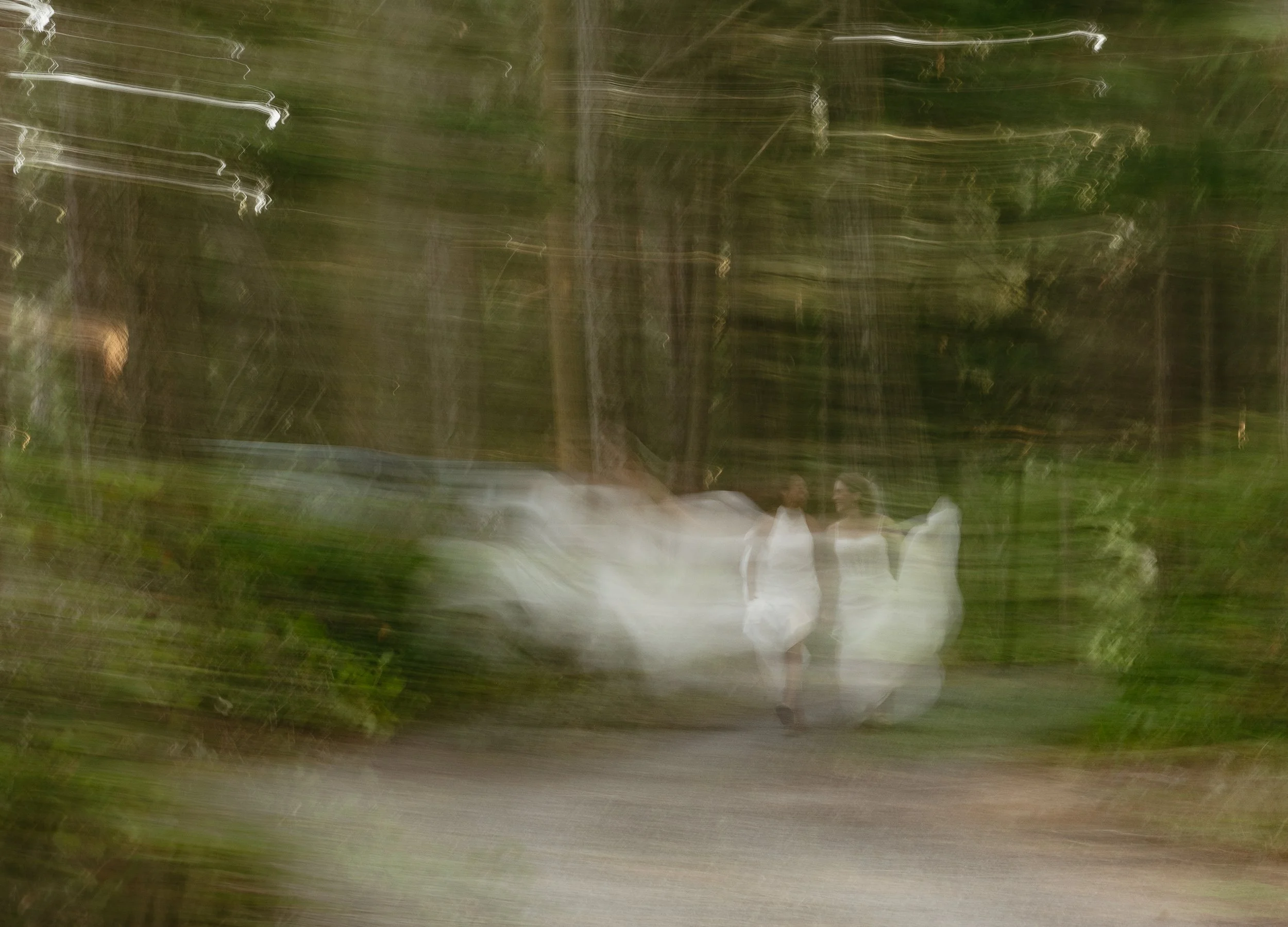 Three women in white dresses walking through a forest with a lot of motion blur.