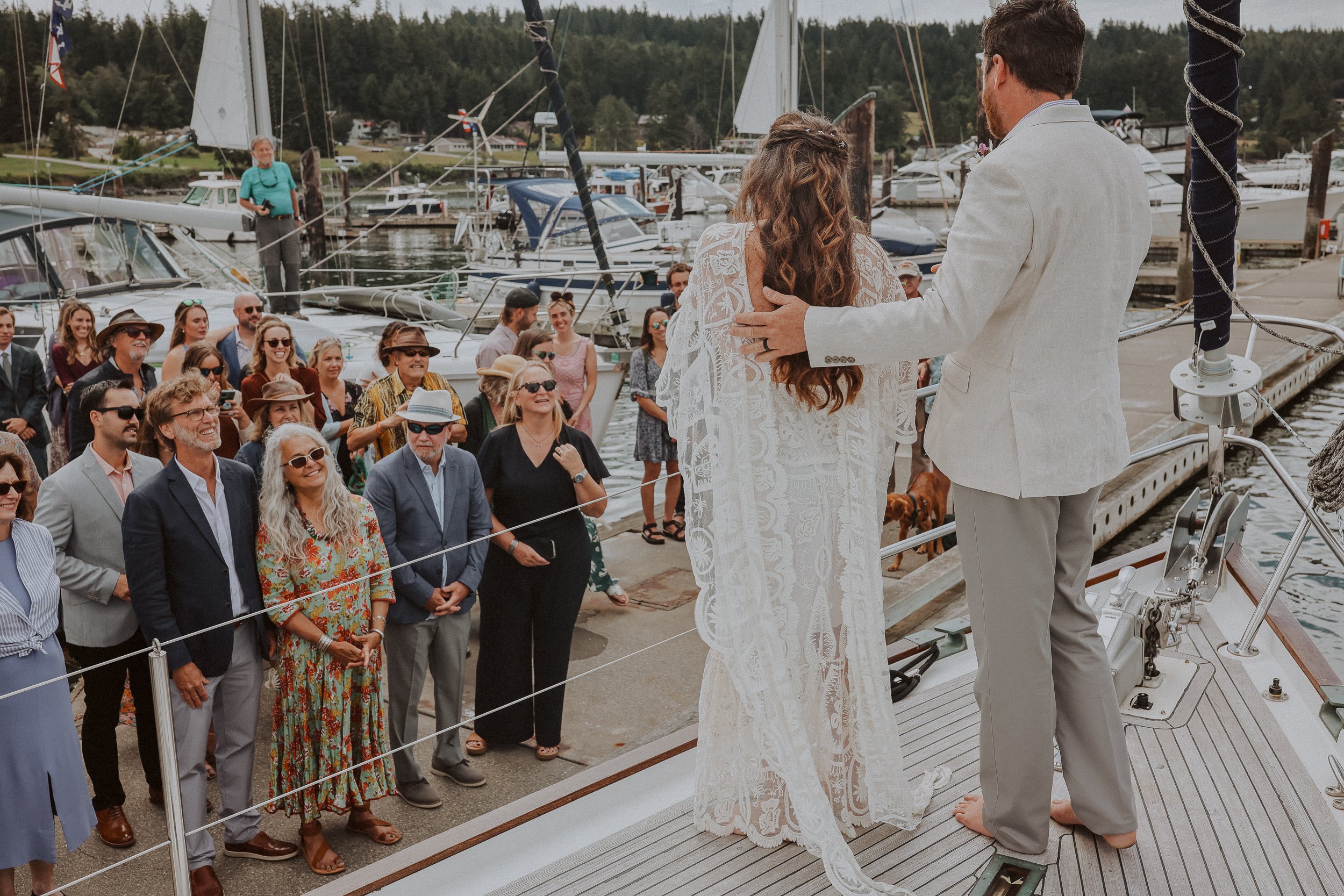A wedding ceremony on a yacht dock with a crowd of guests watching a bride and groom.