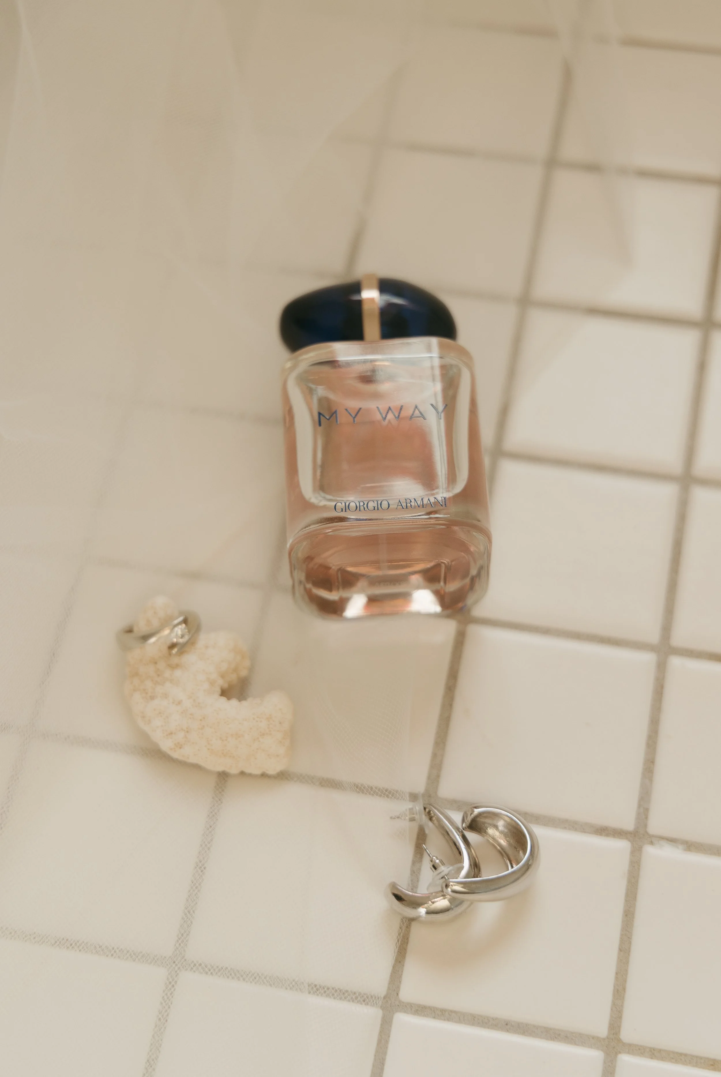 A bottle of Giorgio Armani MY WAY perfume, a white coral shaped ring, and a silver hoop earring on white tiled surface.