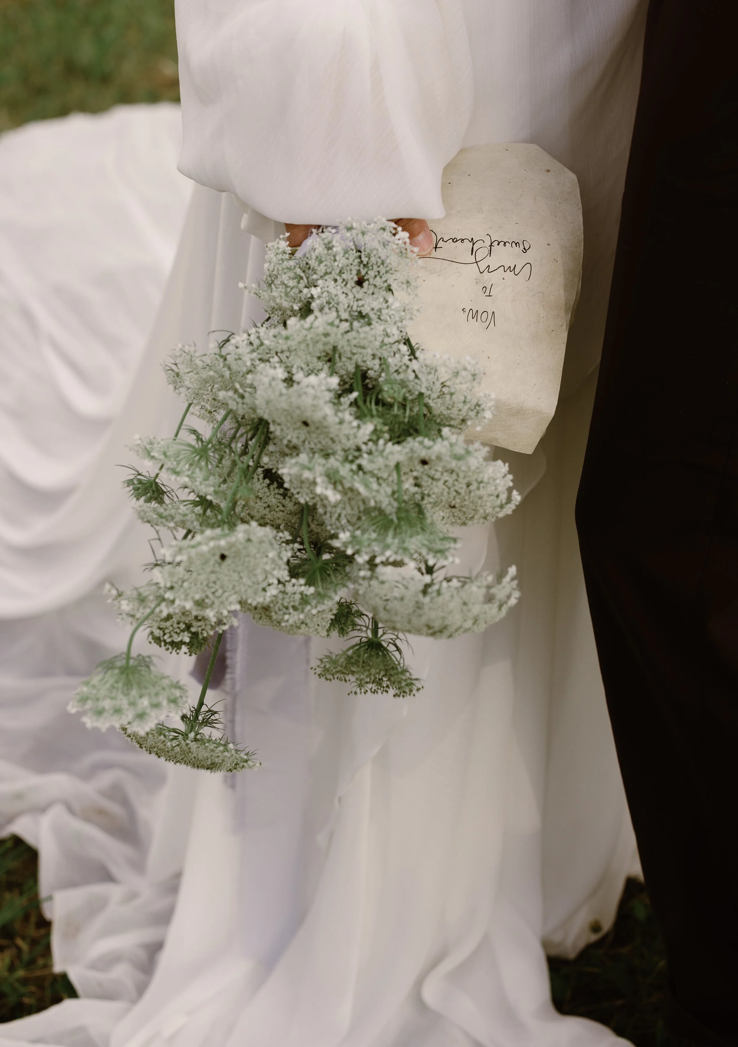 A bride and groom holding a bouquet of white flowers, with a handwritten note on a piece of paper.