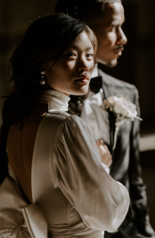 A woman and man dressed formally, possibly at a wedding or special event, with the woman looking directly at the camera and the man looking off to the side.