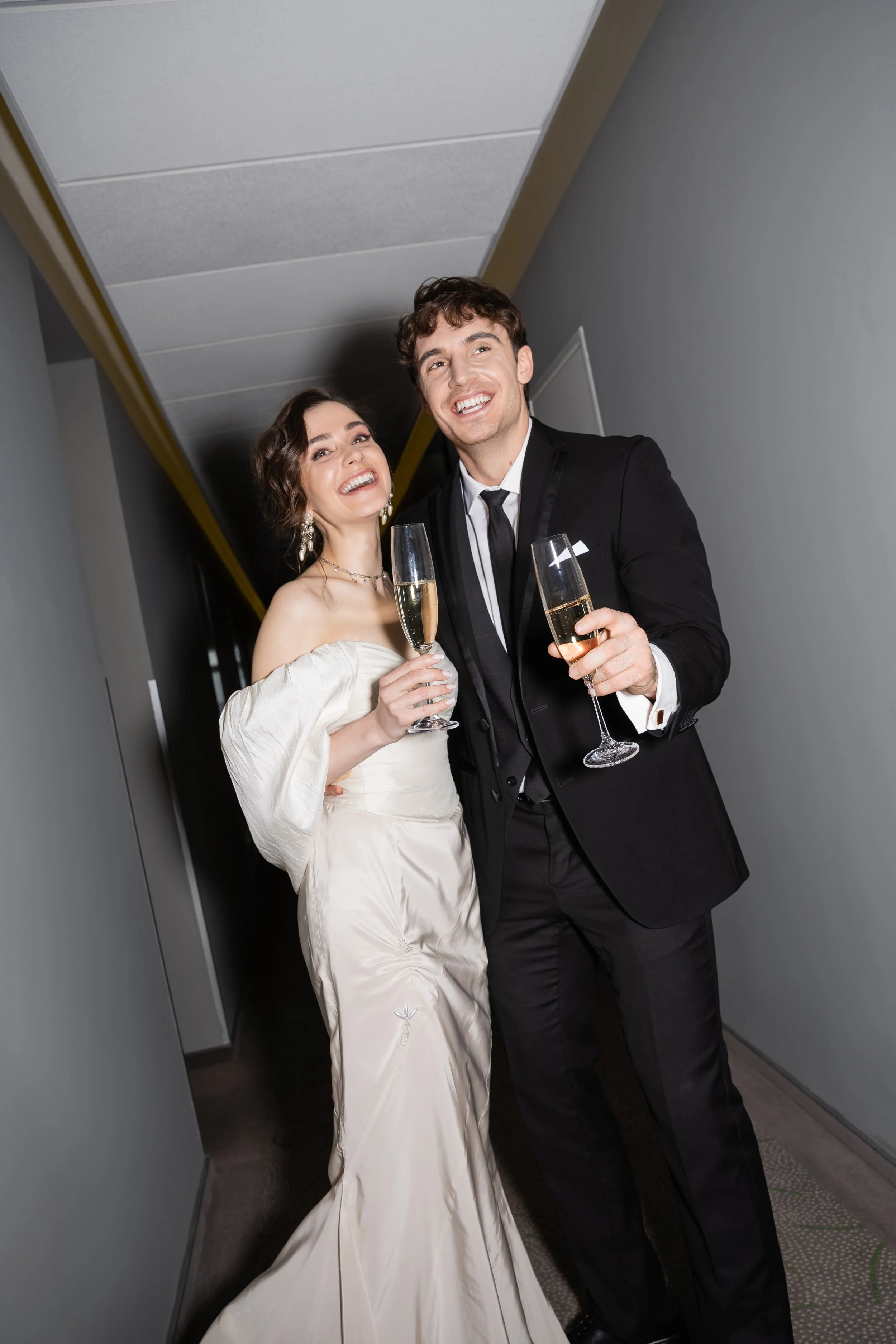 A bride and groom celebrating with champagne in a hallway.